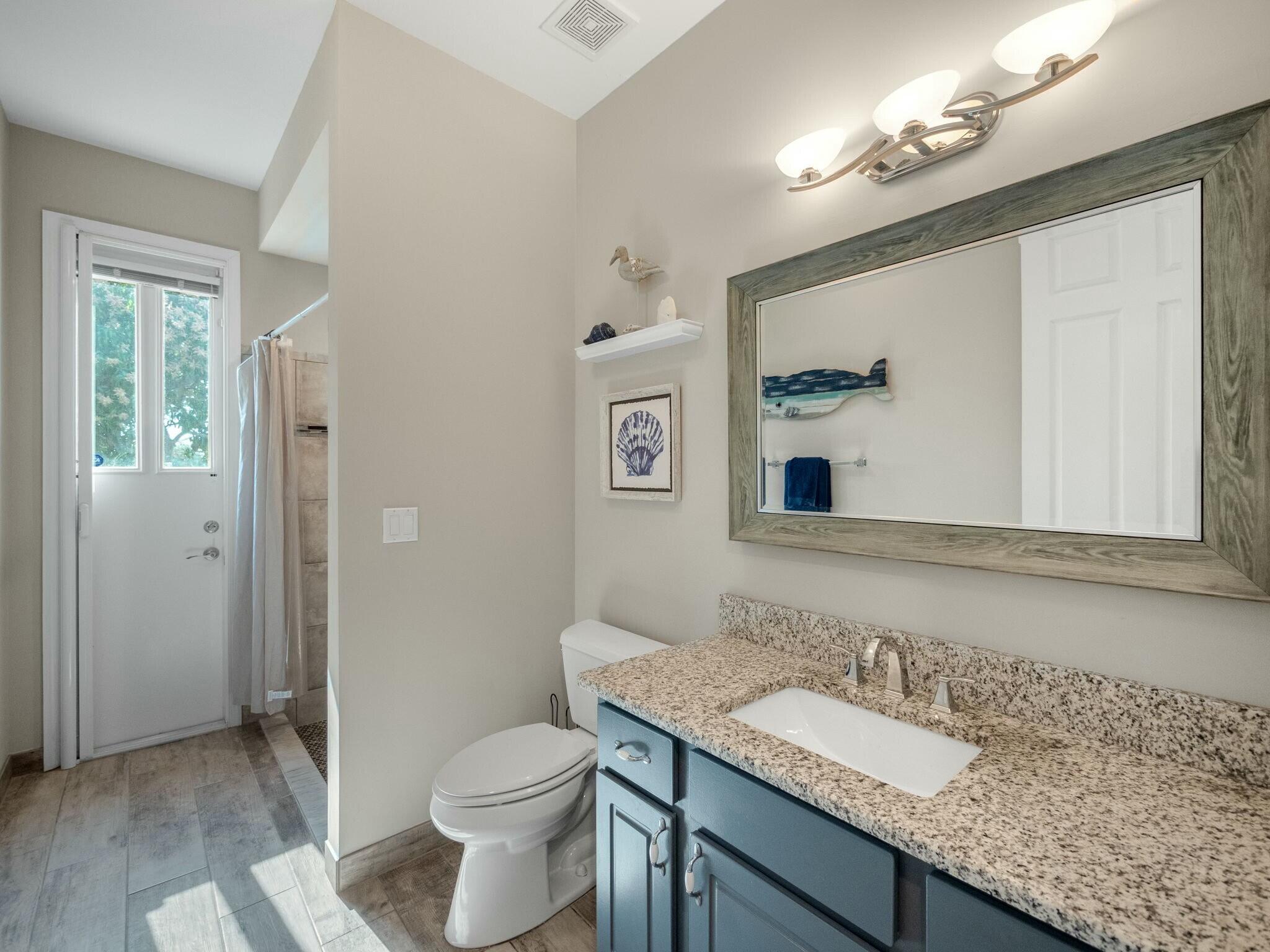 Bathroom with a blue vanity and granite counter, large wood-framed mirror, and glass-paneled door beside the shower.