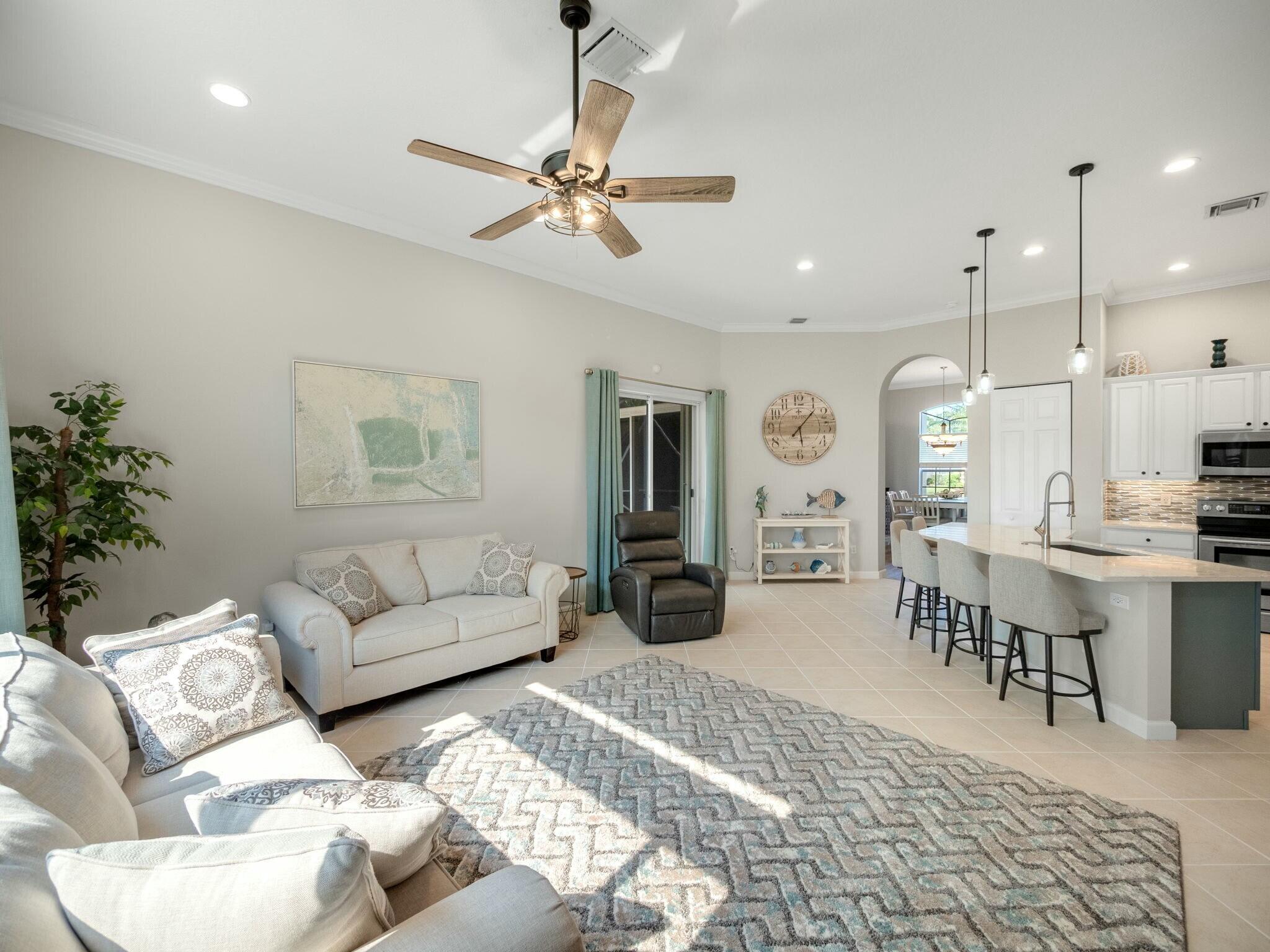 Open-plan living room and kitchen with white sofas, a large patterned rug, and an island with bar seating.