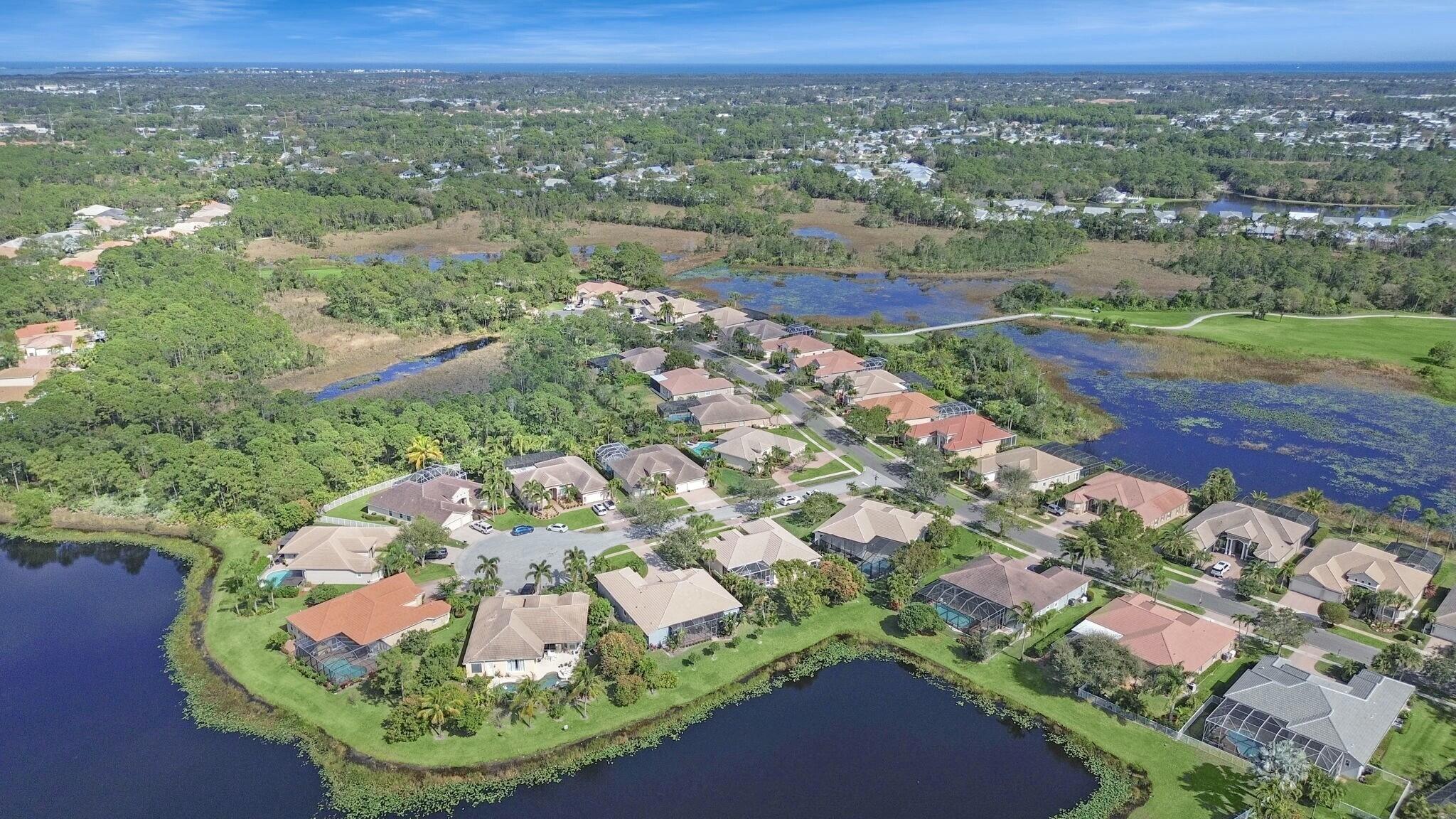 Aerial view of homes beside ponds and wetlands, with a golf course and ocean on the horizon.