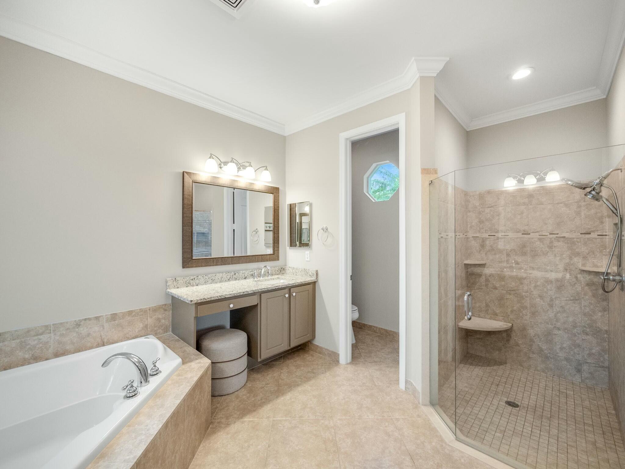 Primary bathroom with a soaking tub, granite vanity, and glass-enclosed tiled walk-in shower.