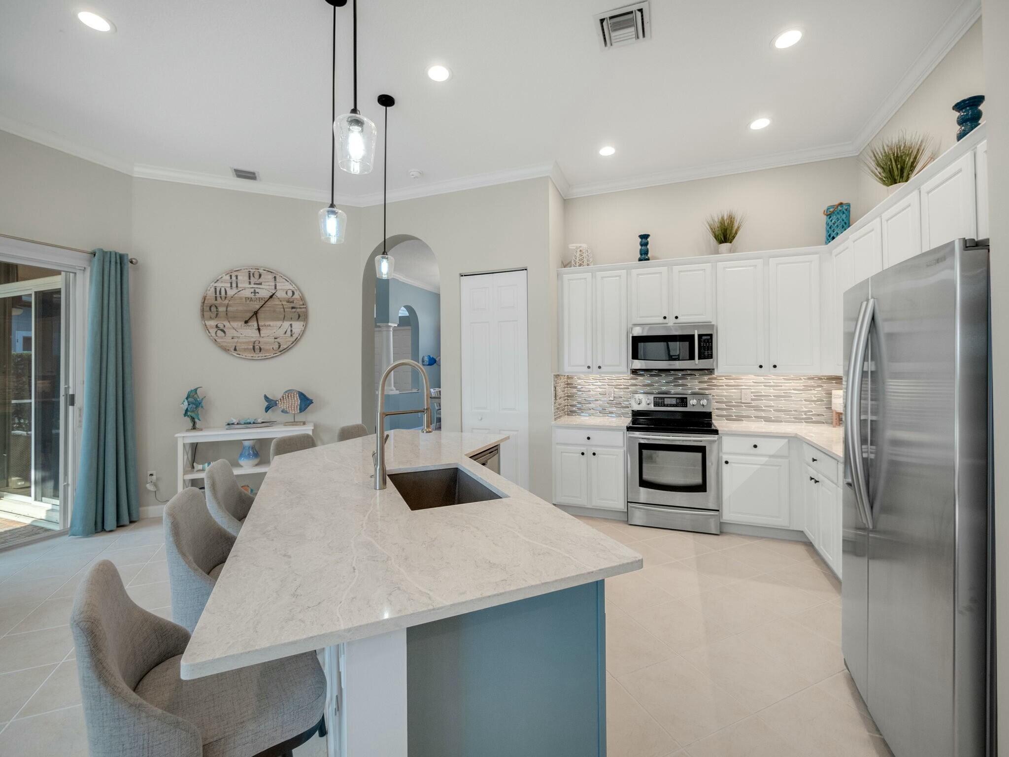 Kitchen with a large blue-based island, white cabinetry, stainless steel appliances and teal curtains.