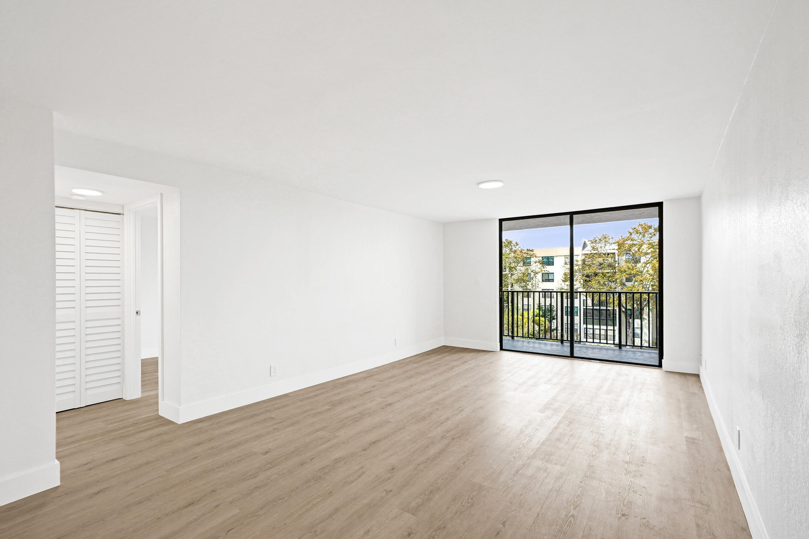 Vacant living room with wood-look floors and sliding glass doors to a balcony.