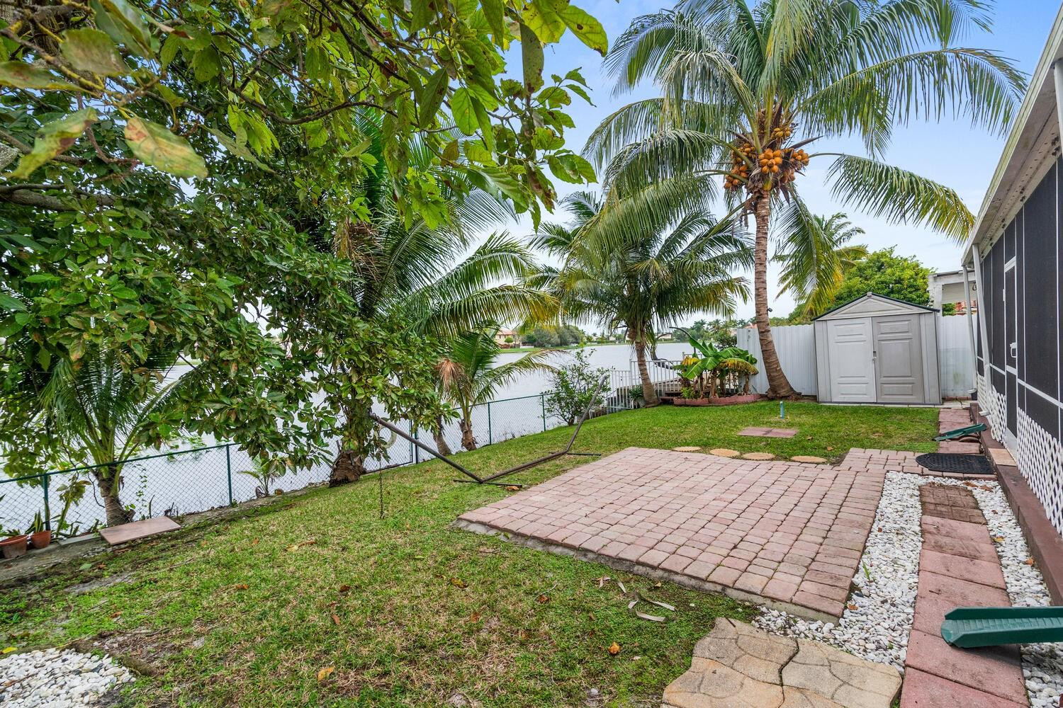 Waterfront backyard with a brick patio, palm trees, and a lawn beside the lake.