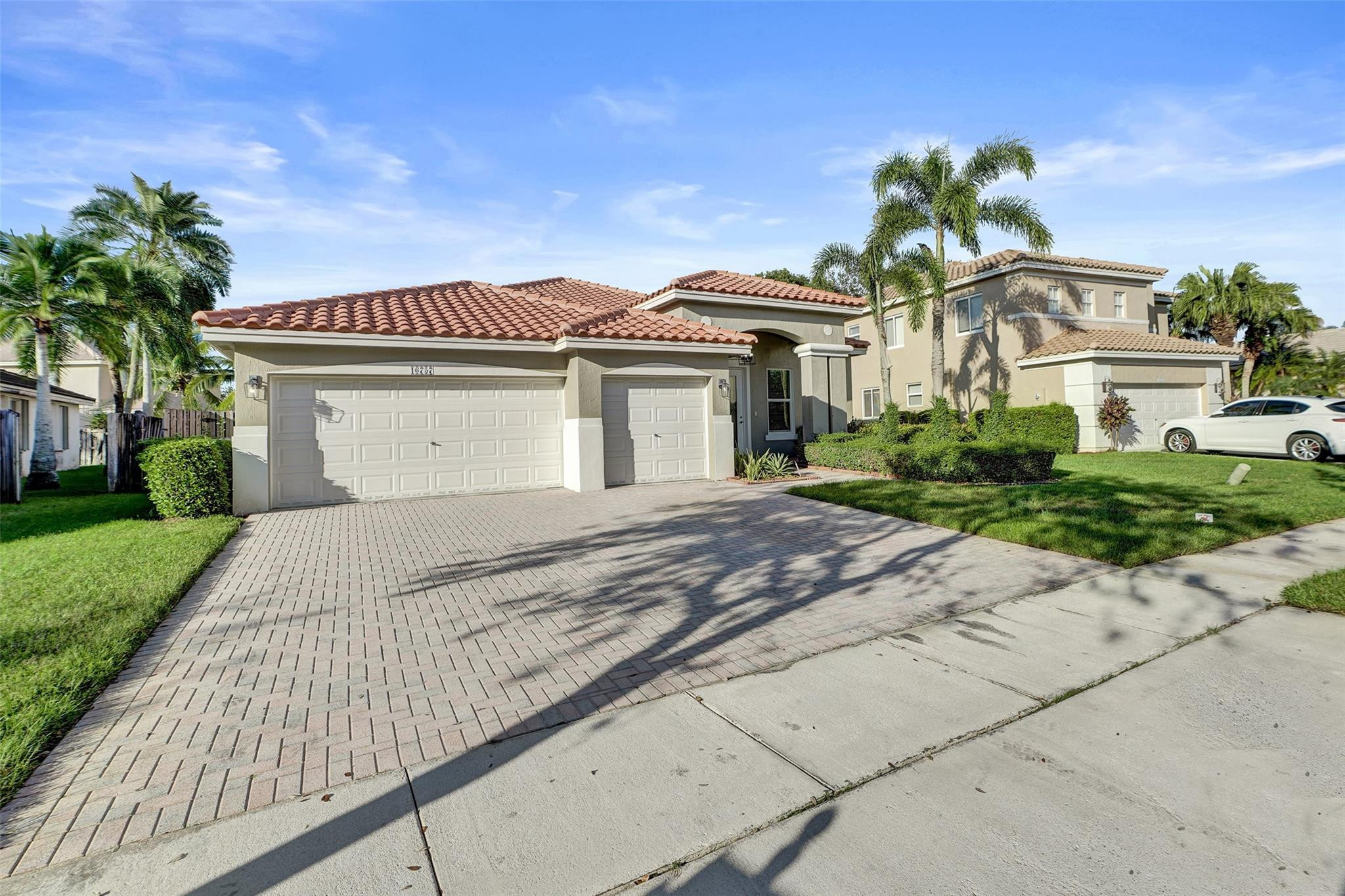 Two-story stucco home with red tile roofs, multiple garages, and a palm-lined driveway.
