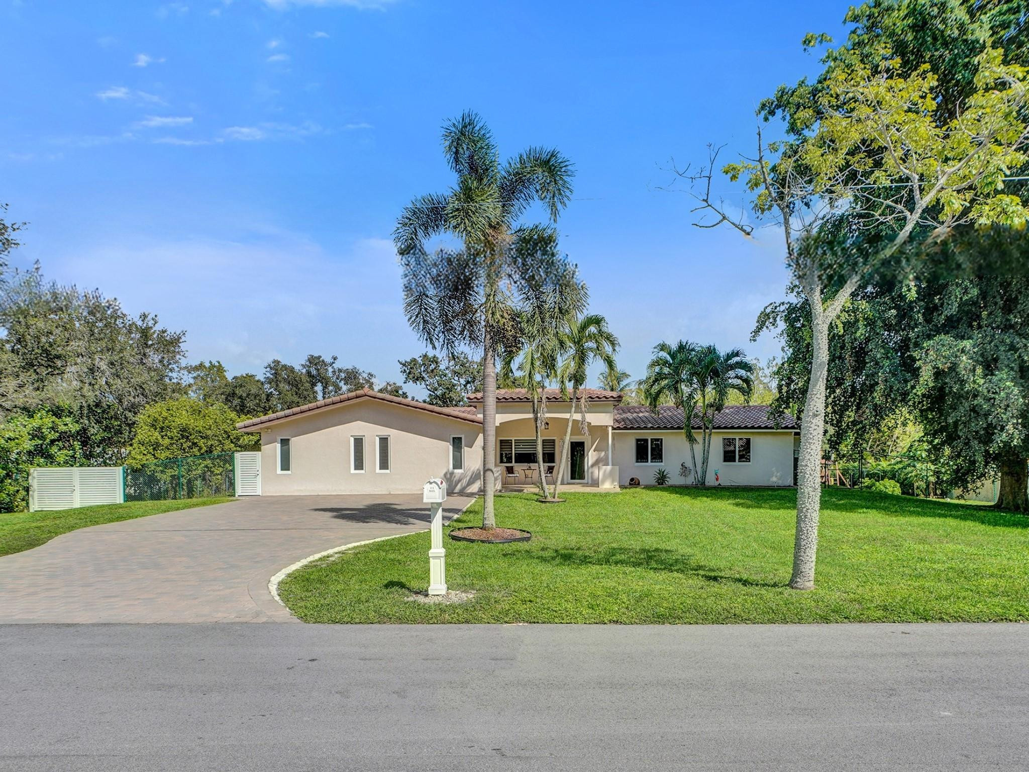Single-story home with a curved driveway, green lawn, and tall palm trees.