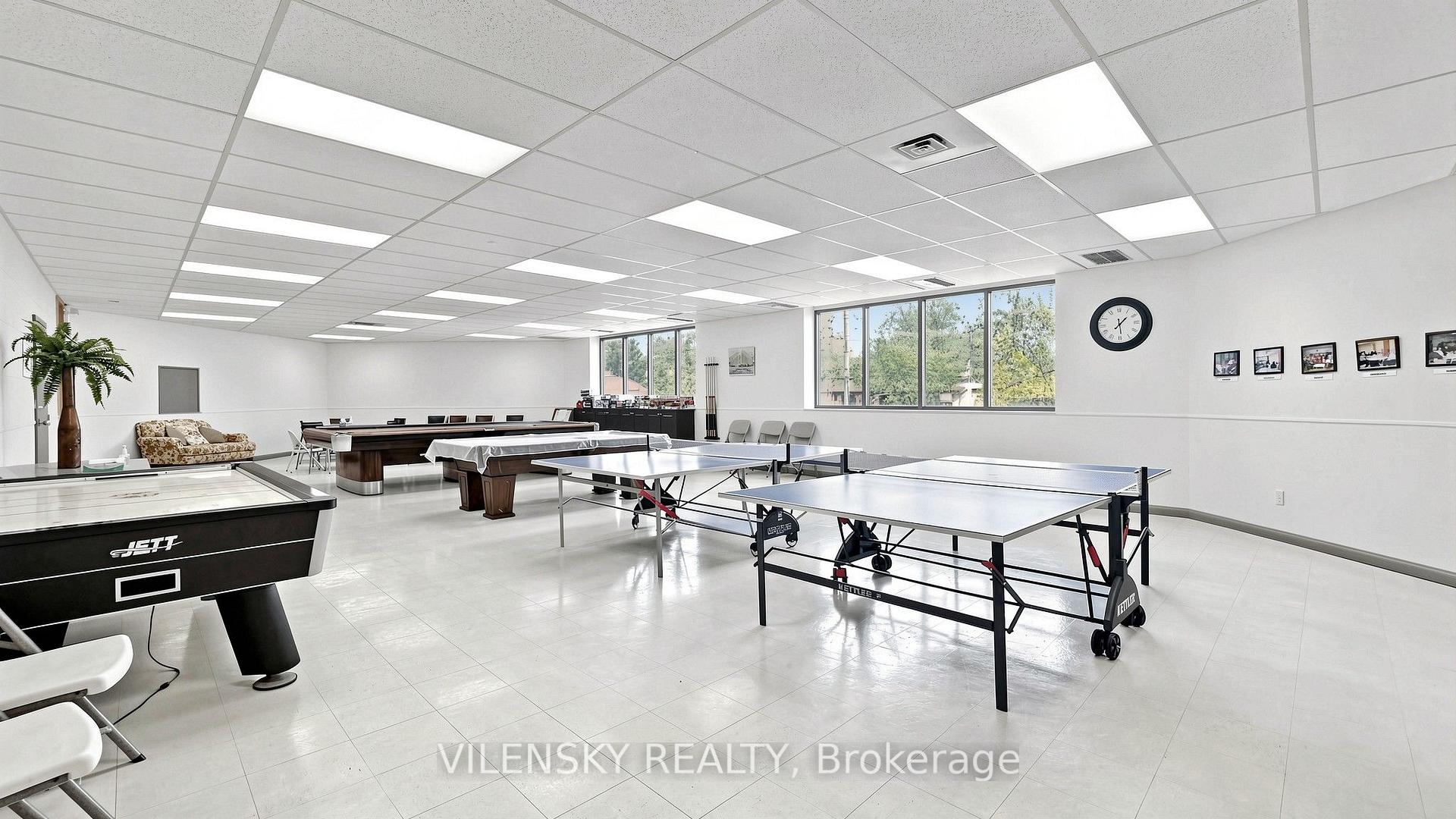 Indoor recreation room with ping-pong tables and a pool table beside large windows.