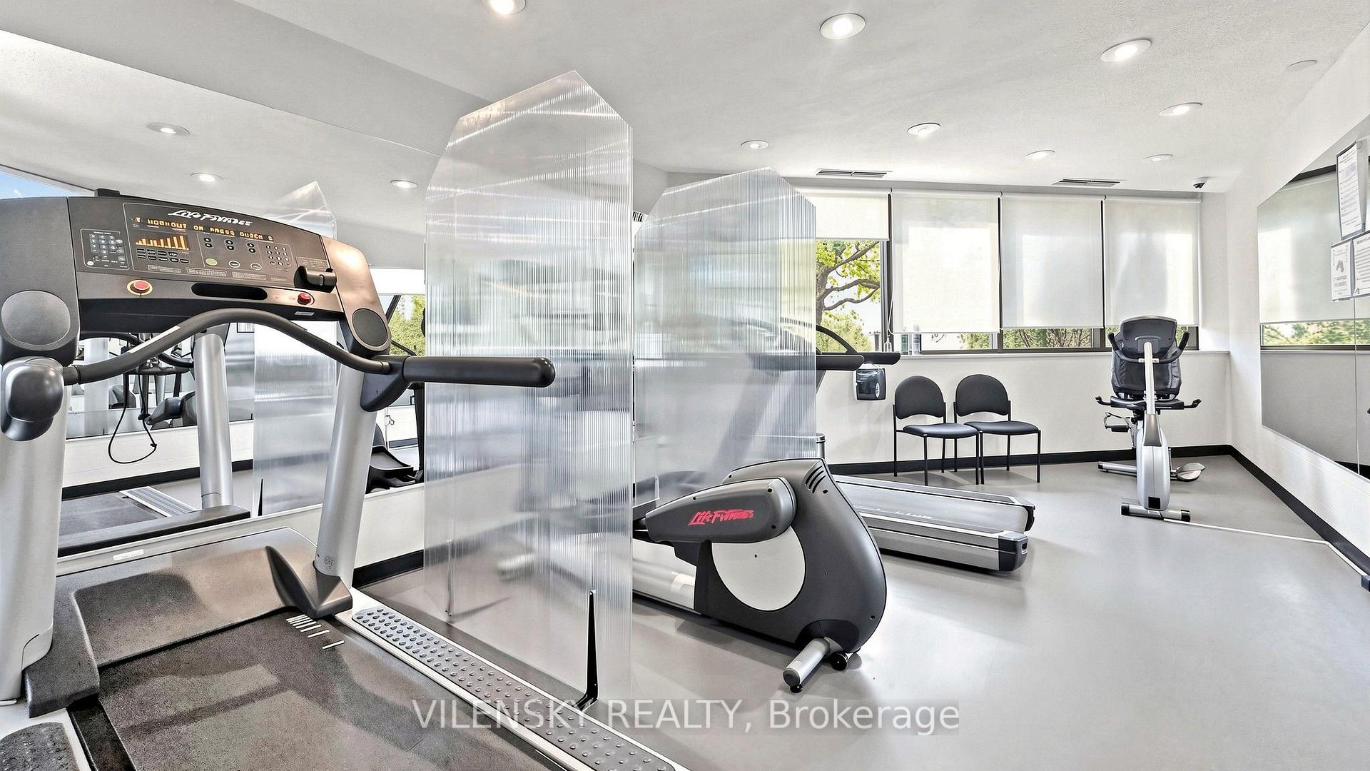 Condominium fitness room with treadmills and stationary bikes beside large windows.