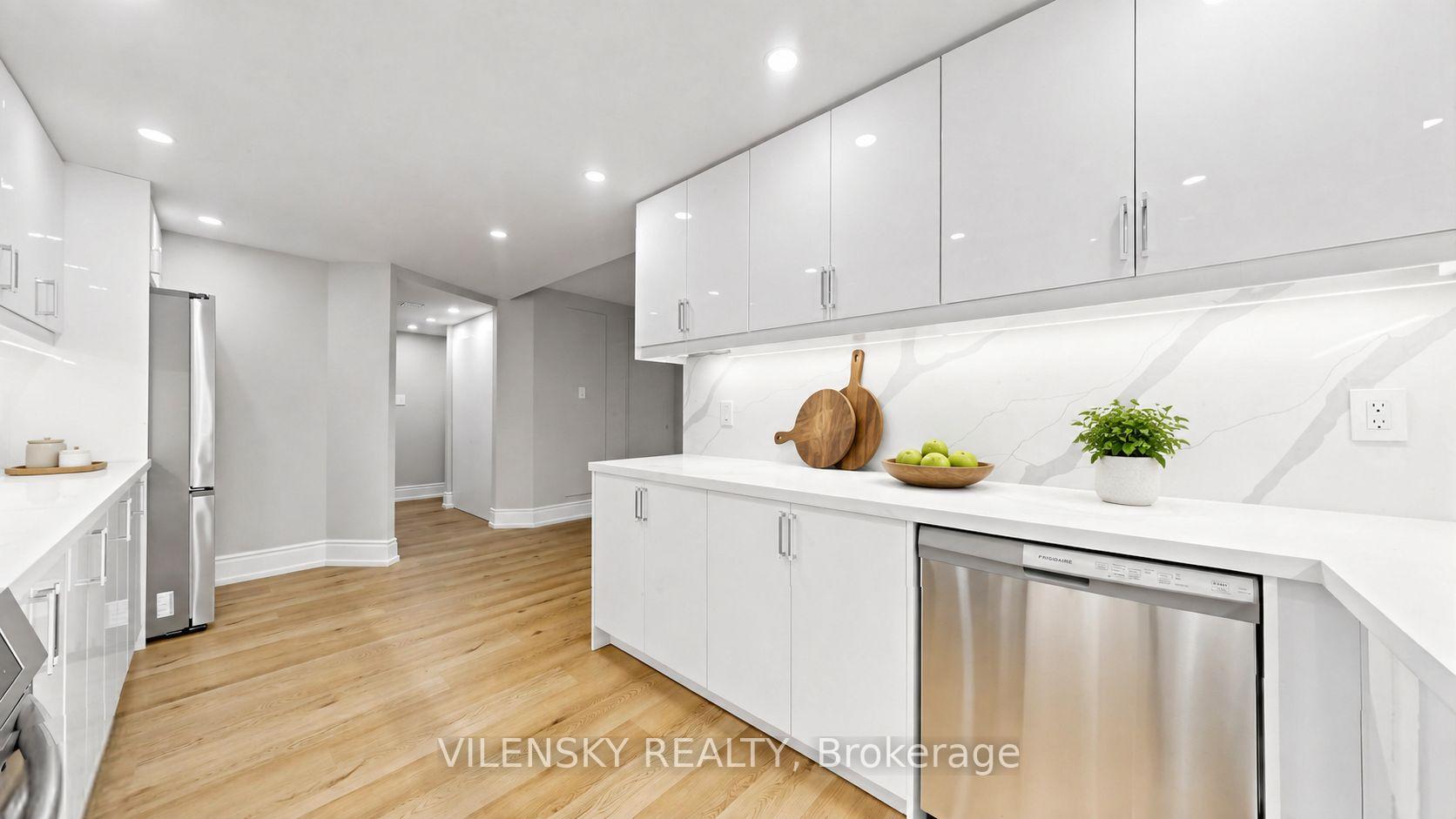 Modern white kitchen with veined backsplash, stainless steel appliances, and light wood floors.