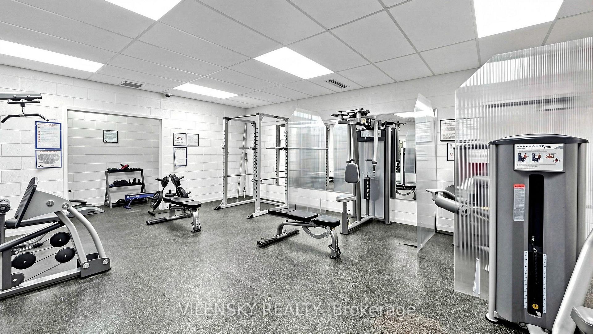 Condominium fitness room with strength-training machines, free weights, mirrors, and gray flooring.