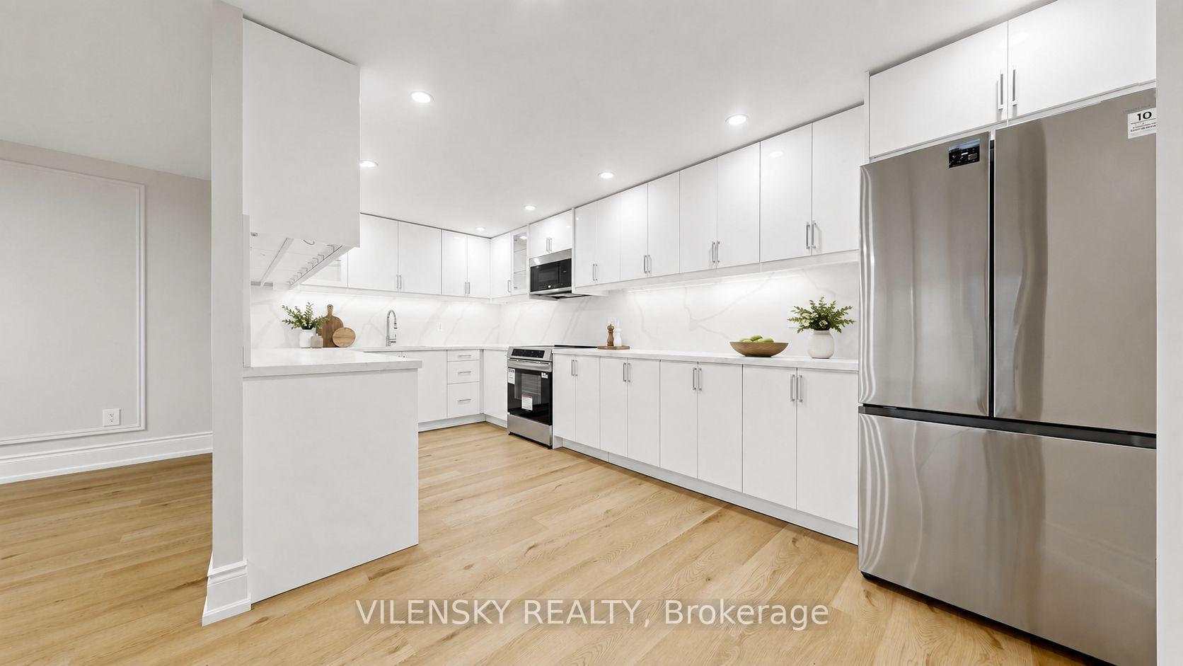 Modern white kitchen with stainless steel appliances and light wood floors.