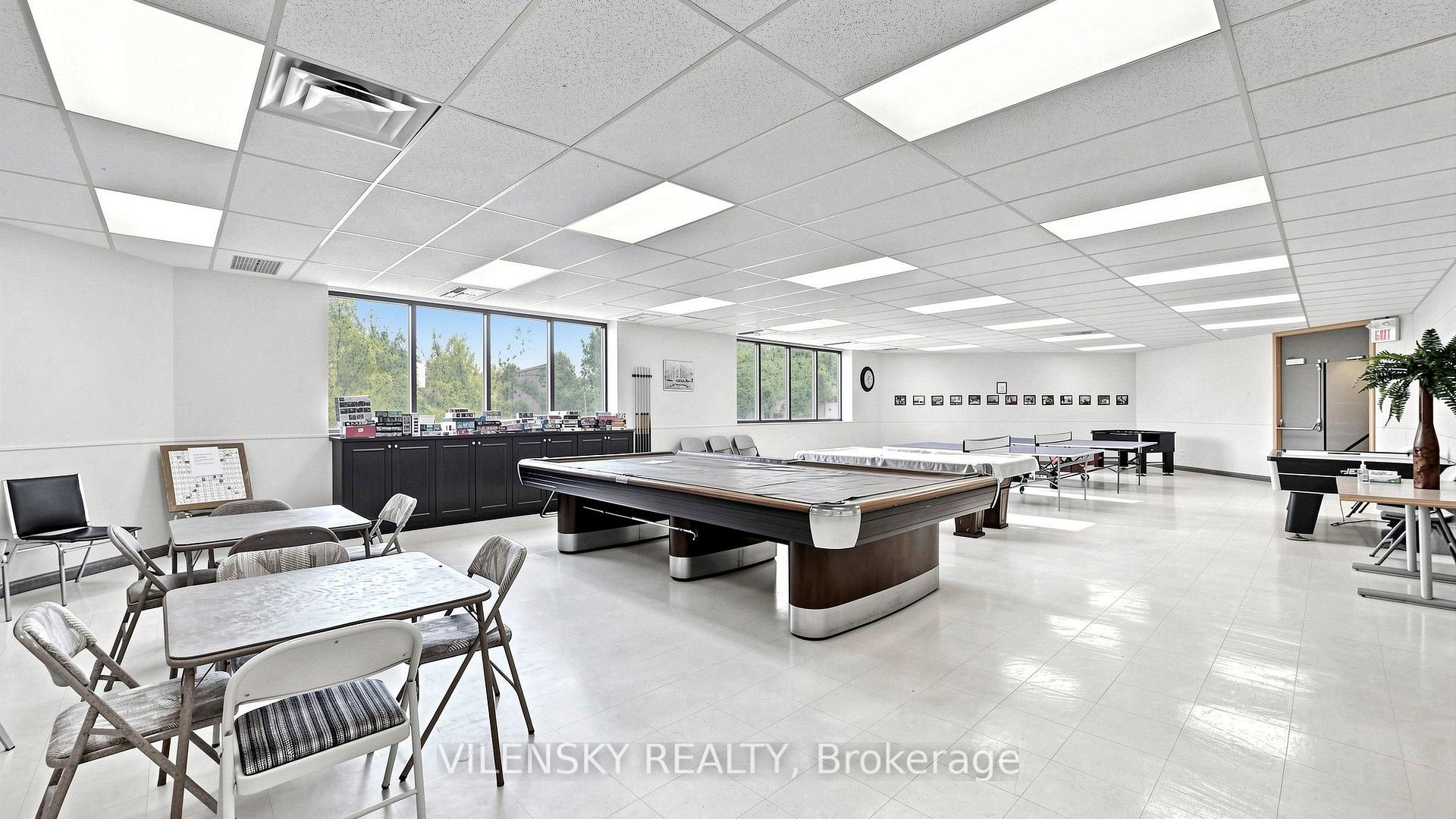 Recreation room with billiards tables, a ping-pong table, and folding tables beside large windows.