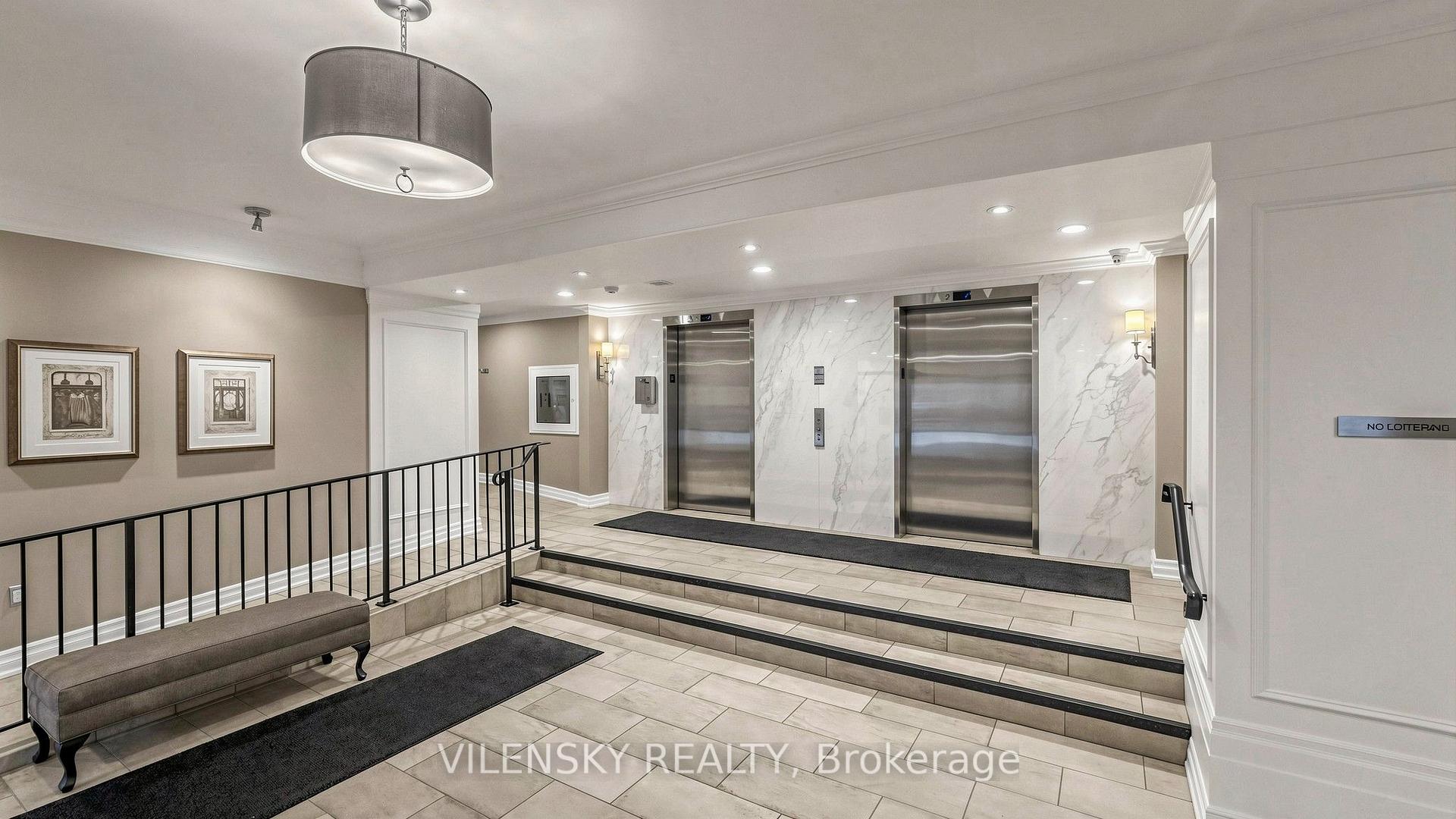Residential building lobby with two elevators, tiled steps, and a bench.