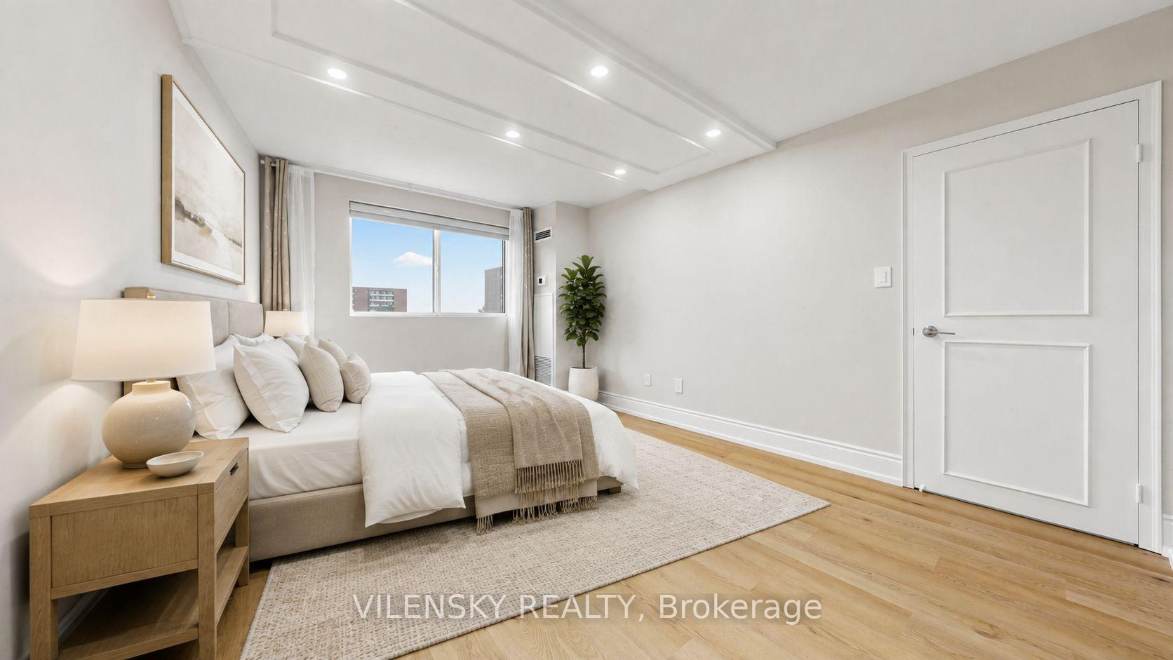 Staged bedroom with a low bed, pale wood floors, and recessed ceiling lights.