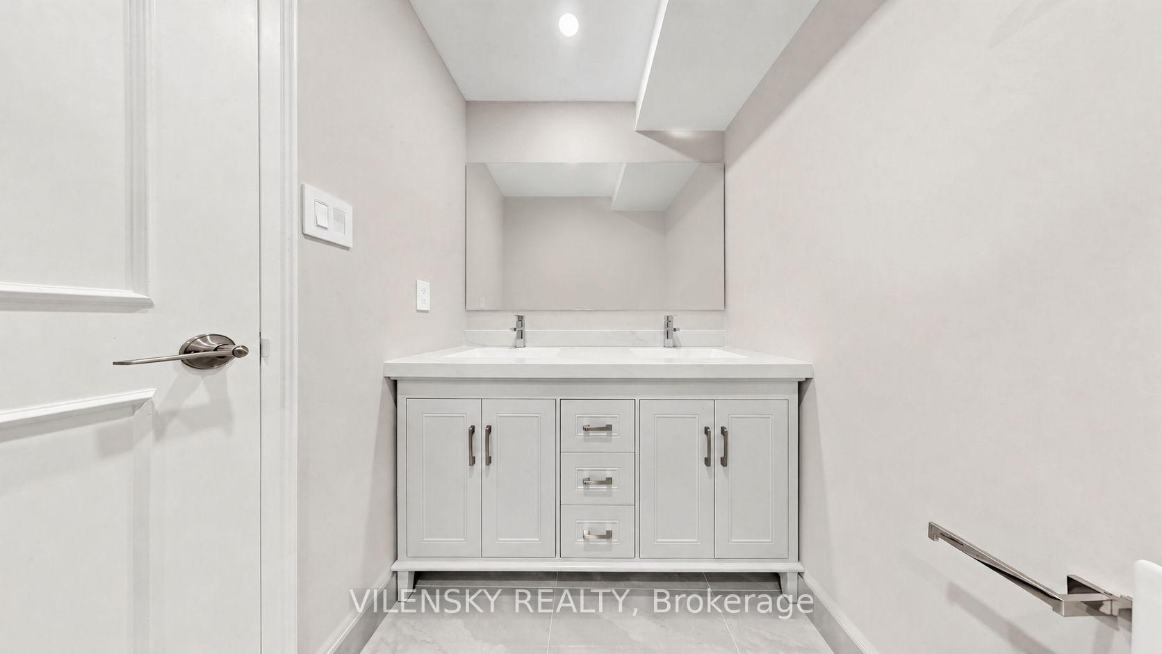 Bathroom with a white double-sink vanity, paneled cabinets, and a large mirror.
