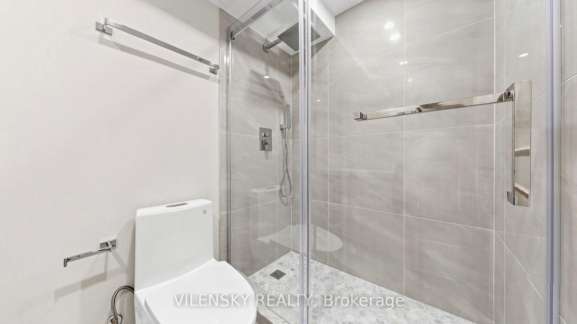 Modern bathroom with a glass walk-in shower, gray tile, mosaic floor, and white toilet.