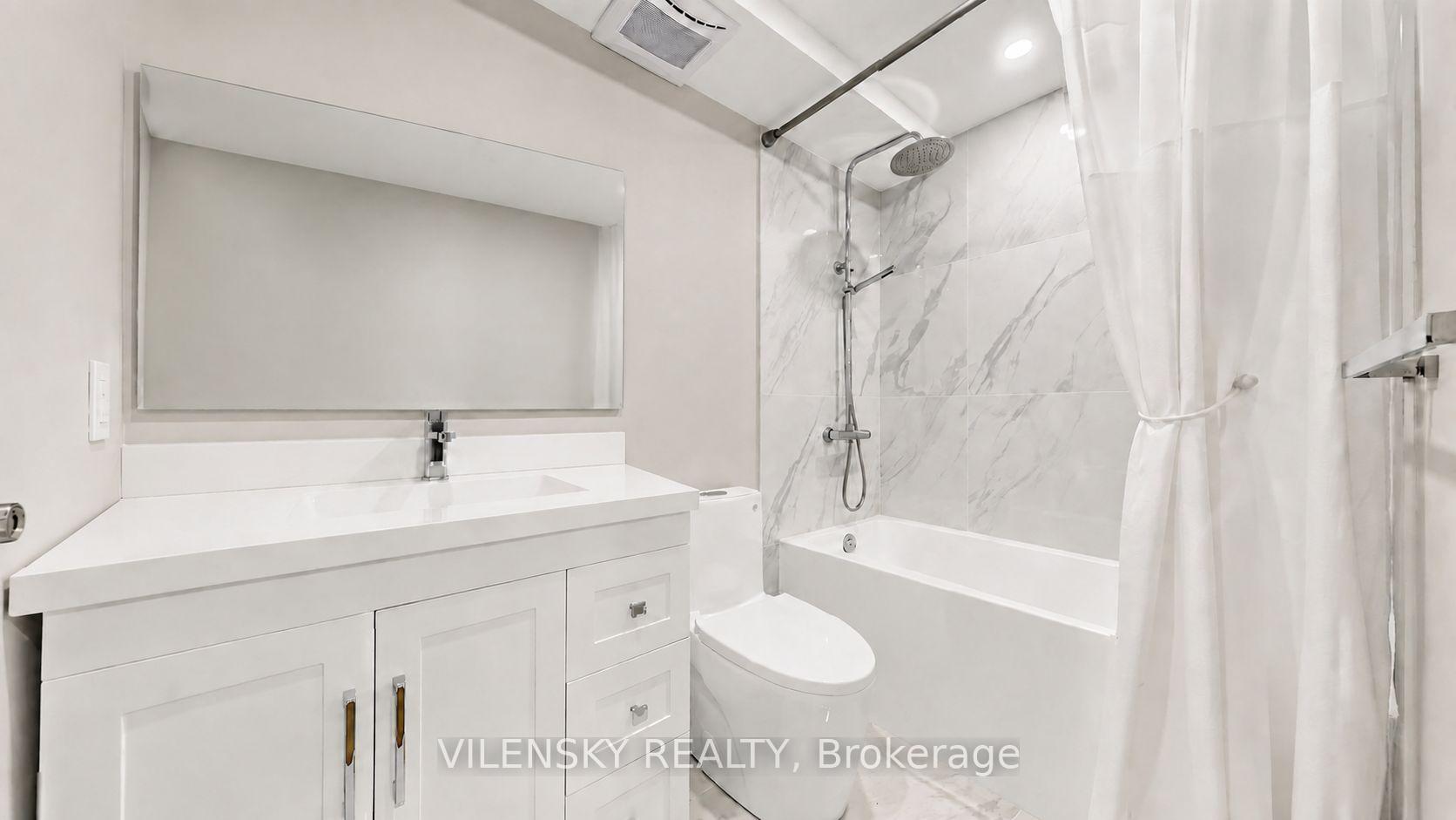 Bathroom with a white vanity, large mirror, and marble-look tub-shower surround.