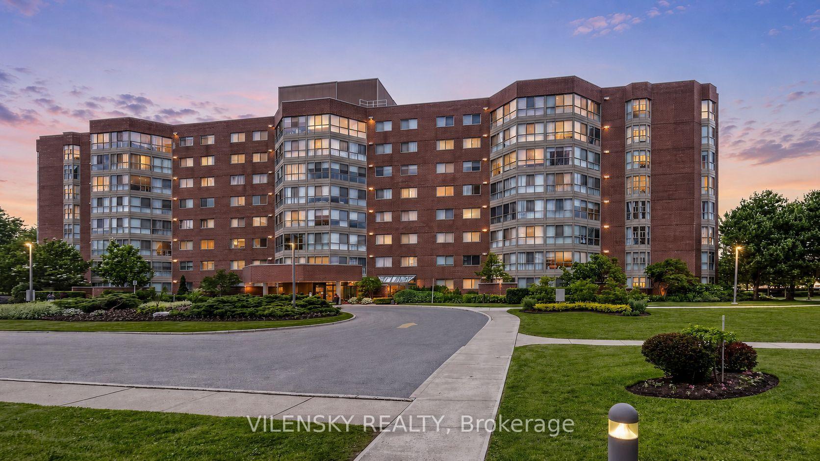 Red-brick condominium with curved glass balconies and landscaped grounds at dusk.