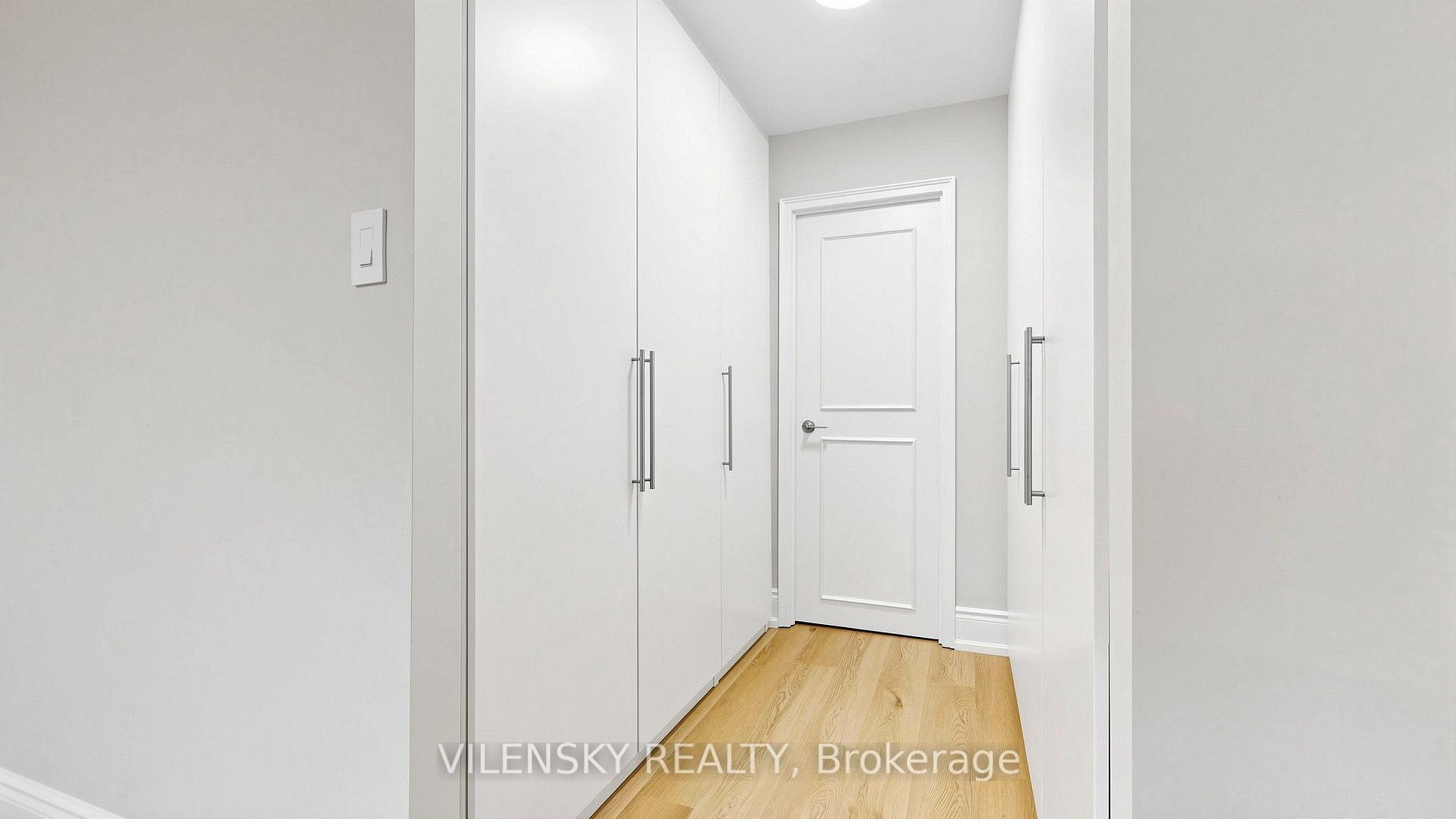Bright hallway with white built-in closets, light wood flooring, and a paneled door.