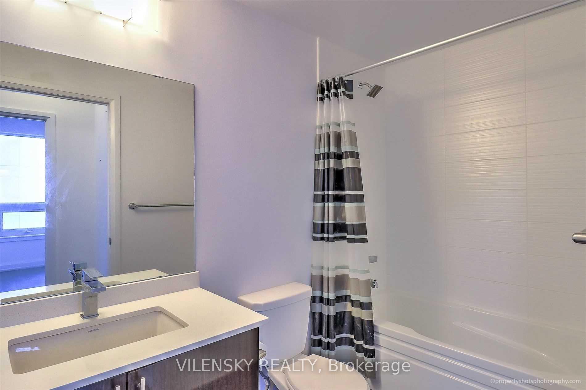 Condo bathroom with a striped shower curtain, white bathtub, toilet, and vanity with integrated sink.