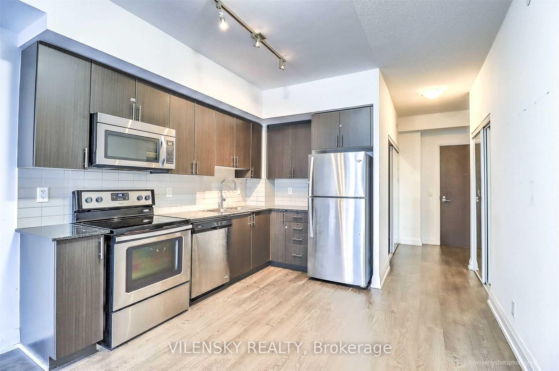 Condo kitchen with dark cabinets, stainless steel appliances, and light wood flooring.