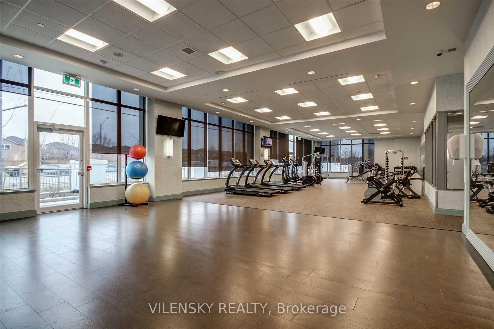Condominium fitness room with treadmills, weight machines, large windows, and colorful exercise balls.