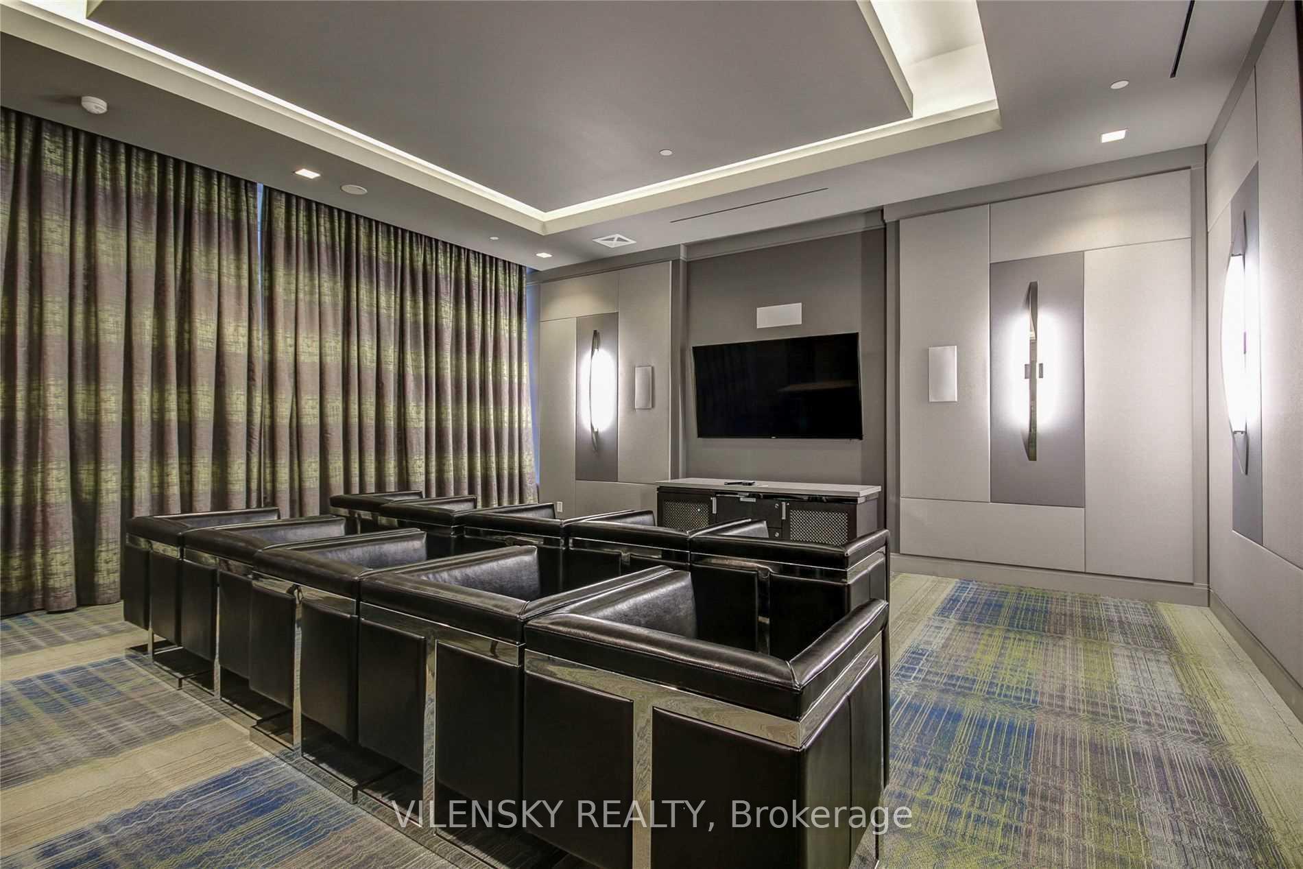 Condominium media room with rows of black leather theater seats facing a wall-mounted television.