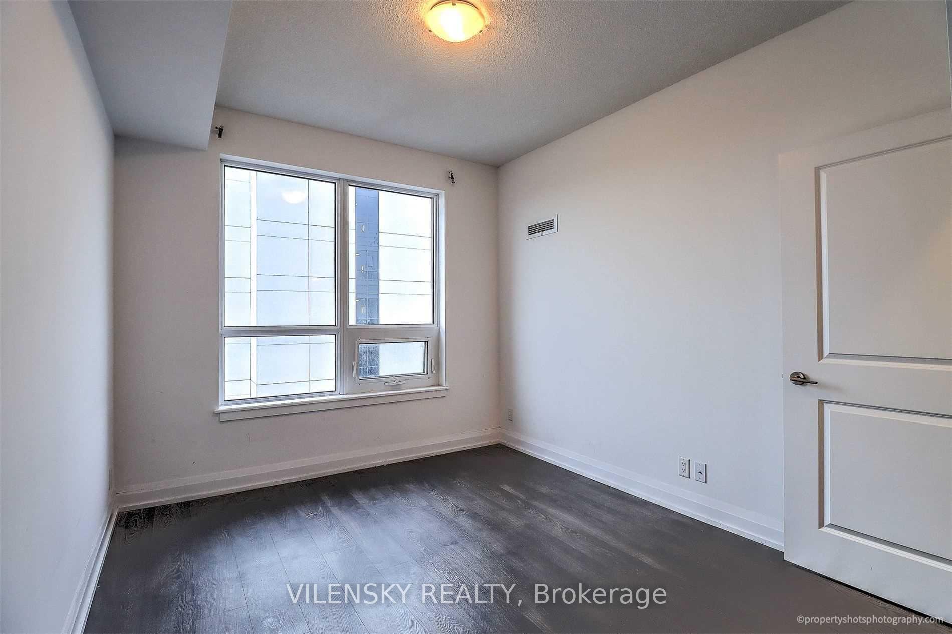 Empty condominium room with dark flooring and a large window