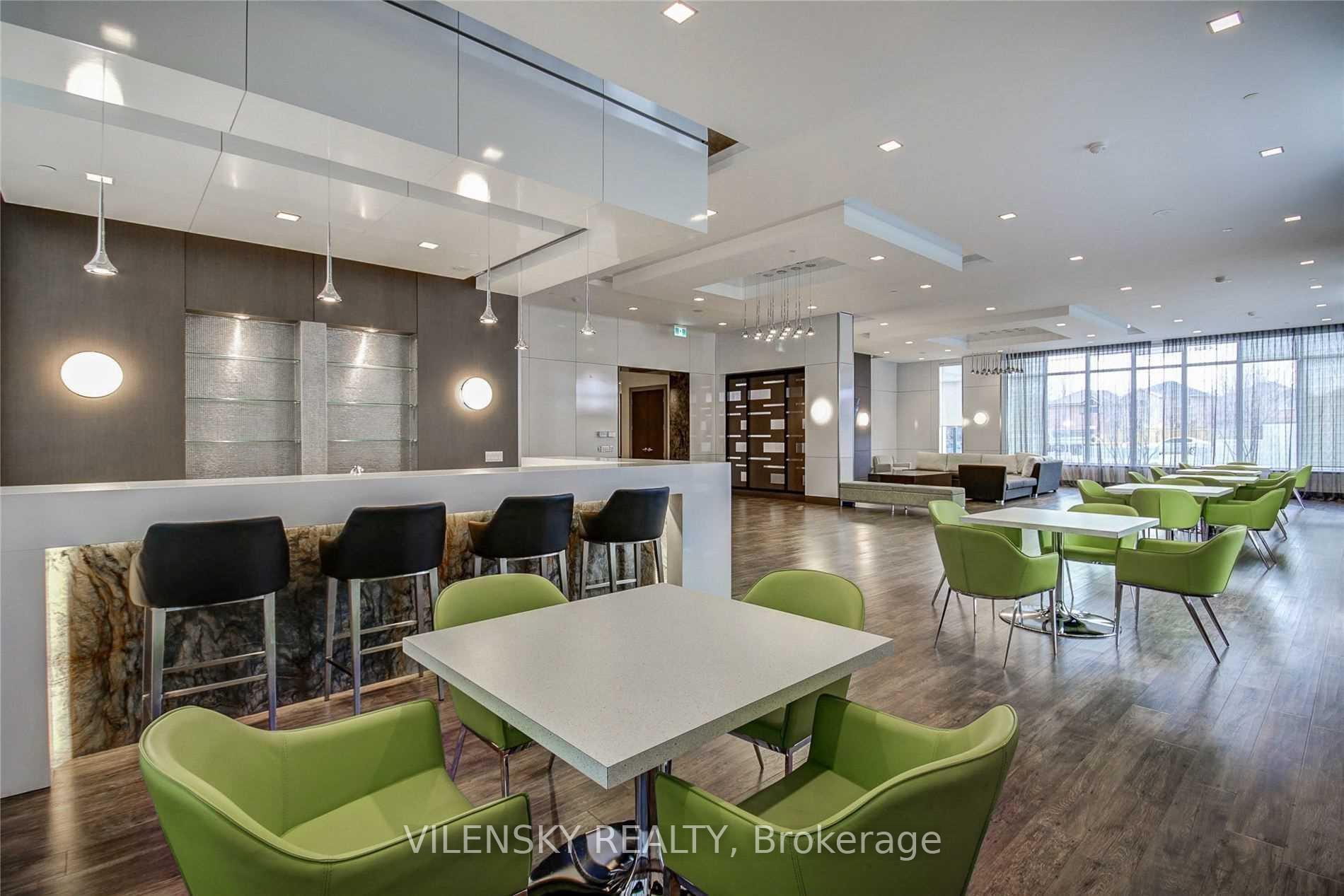 Condominium lounge with a bar counter, black stools, green chairs, and large curtained windows.