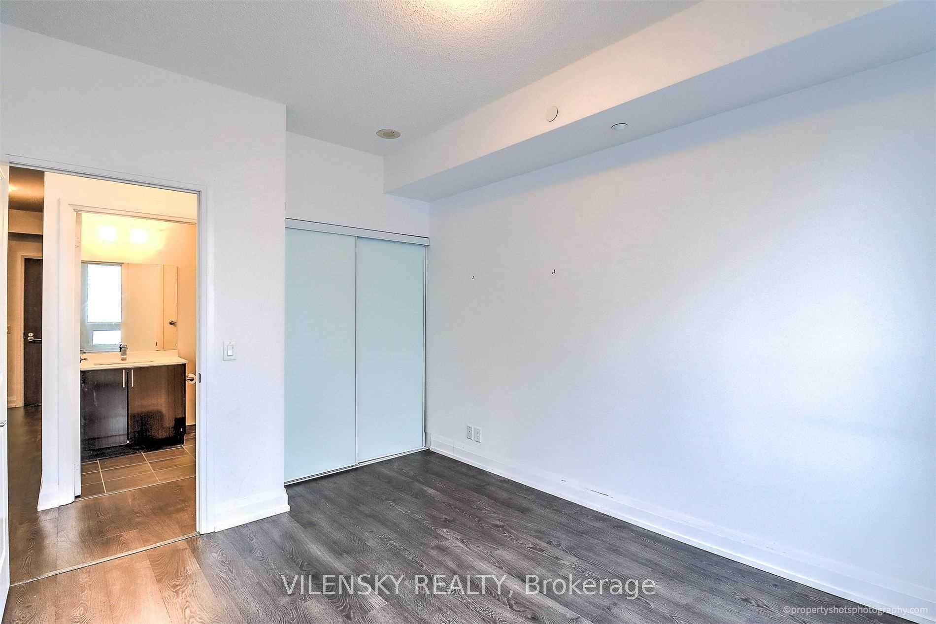 Empty condo bedroom with sliding closet doors and an open doorway to the bathroom.