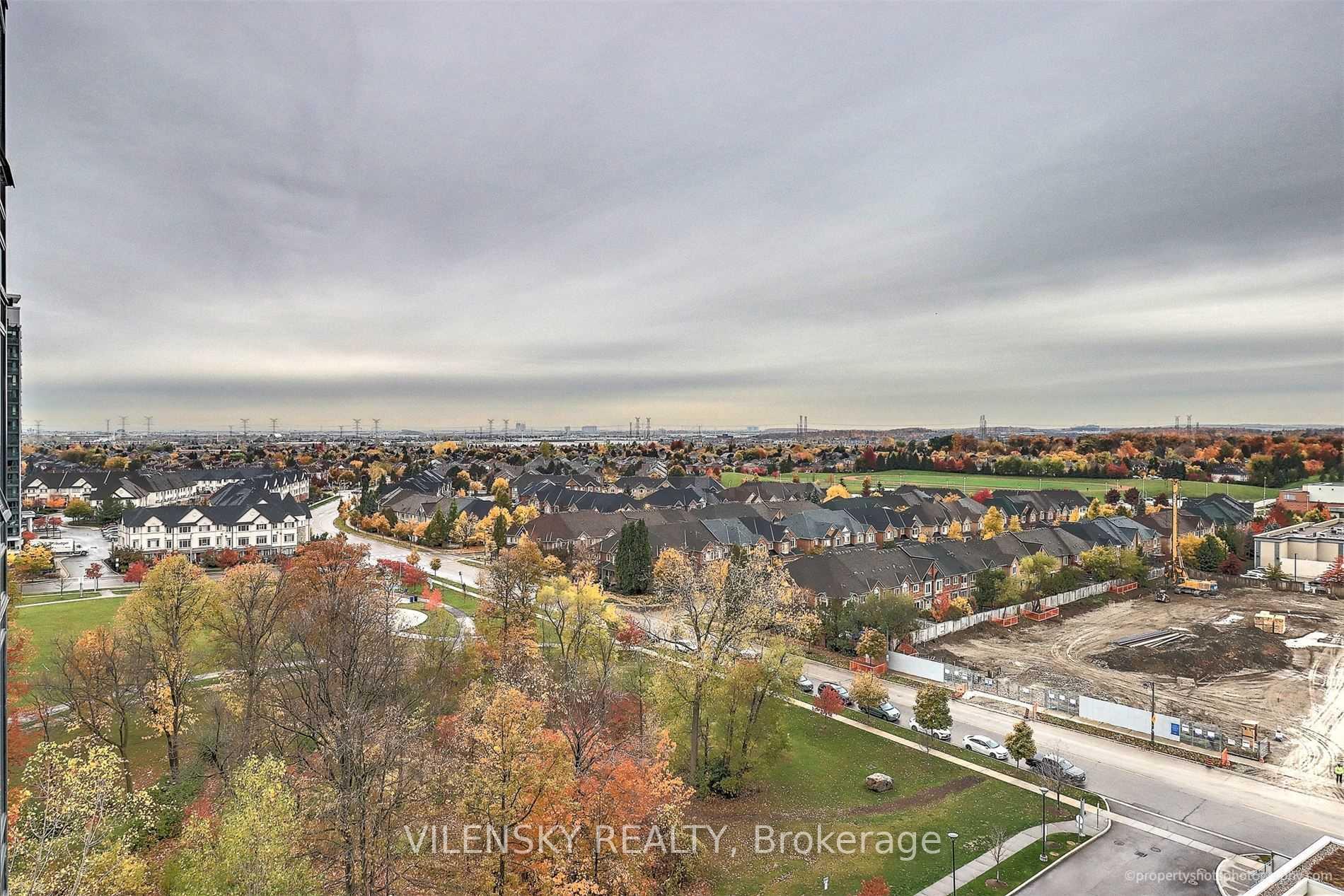 Panoramic autumn view over suburban homes, parkland, and a construction site beneath an overcast sky.