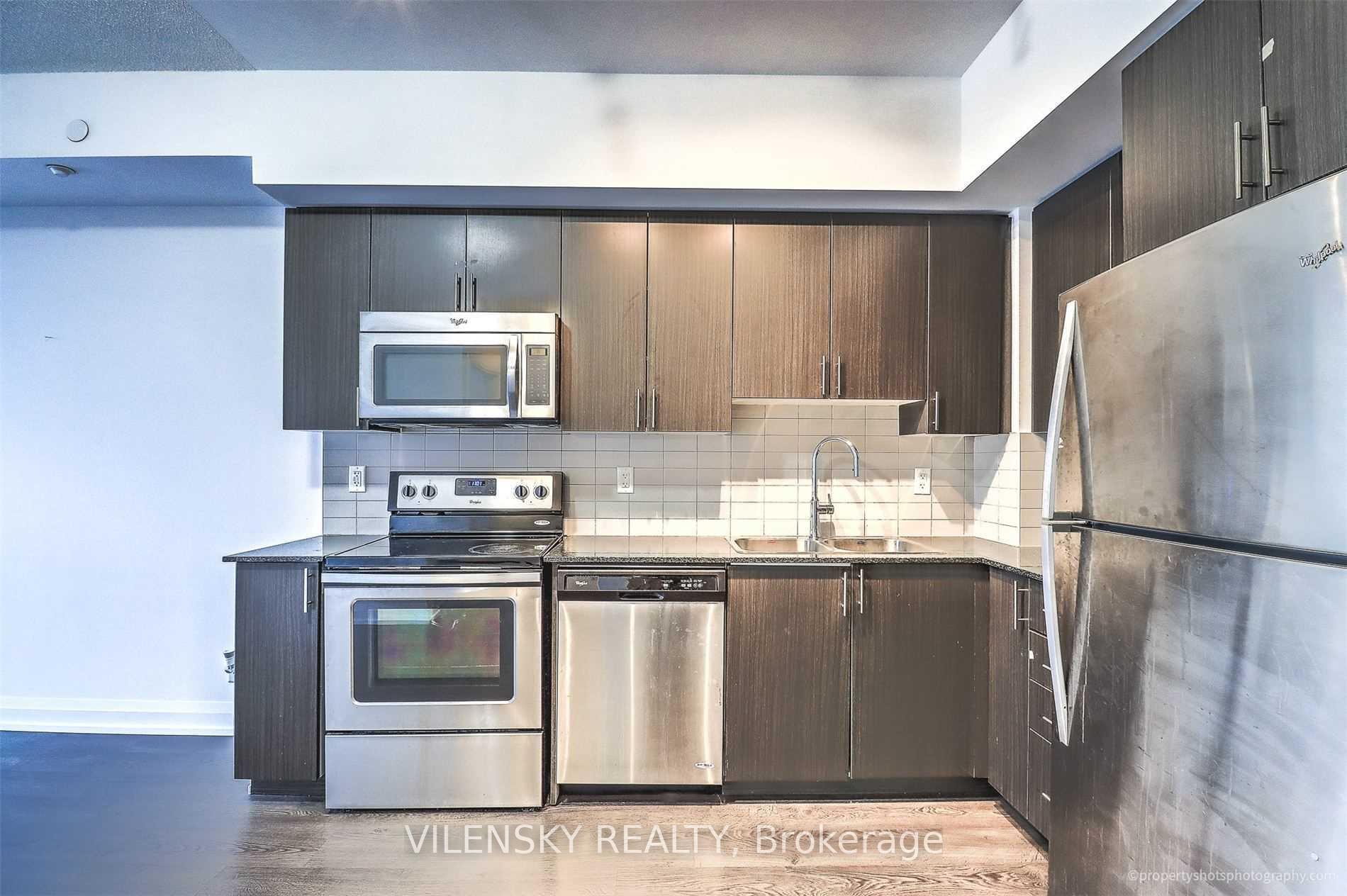 Condo kitchen with dark wood cabinetry, stainless steel appliances, tiled backsplash, and a double-basin sink.