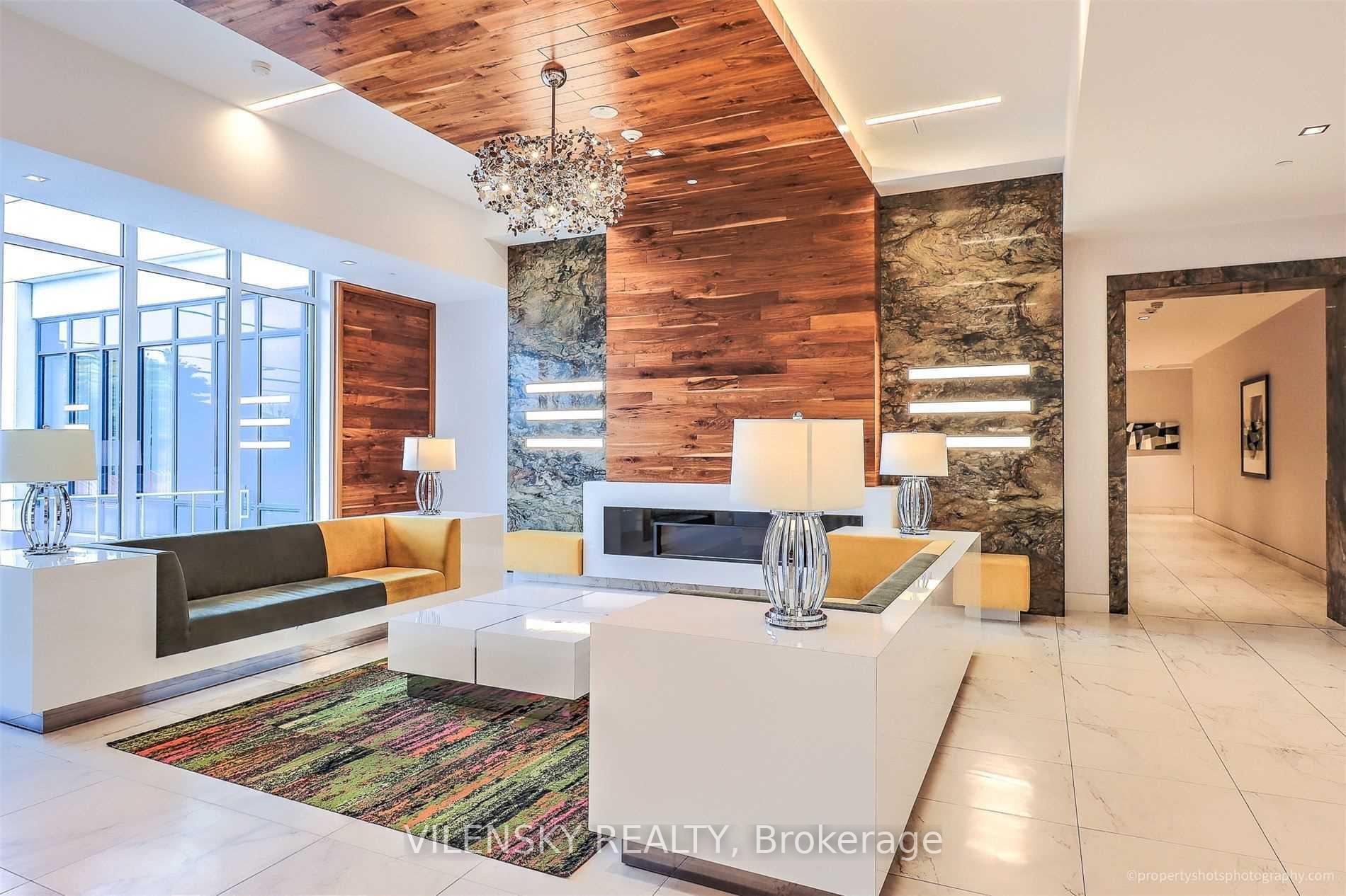 Condominium lobby lounge with a wood-paneled fireplace wall, stone accents, and colorful rug.