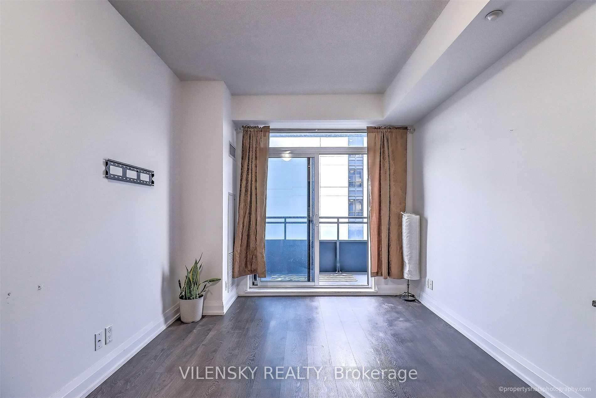 Unfurnished condo living room with dark wood floors, brown curtains, and a sliding glass door to the balcony.