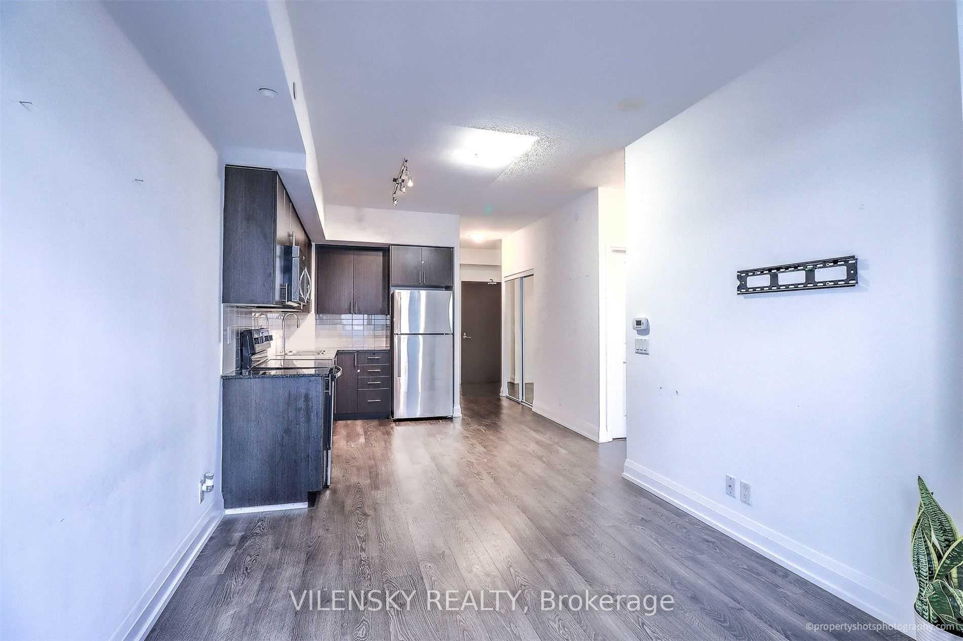 Open-plan condo kitchen and living area with dark cabinetry, stainless refrigerator, and wood-look flooring.