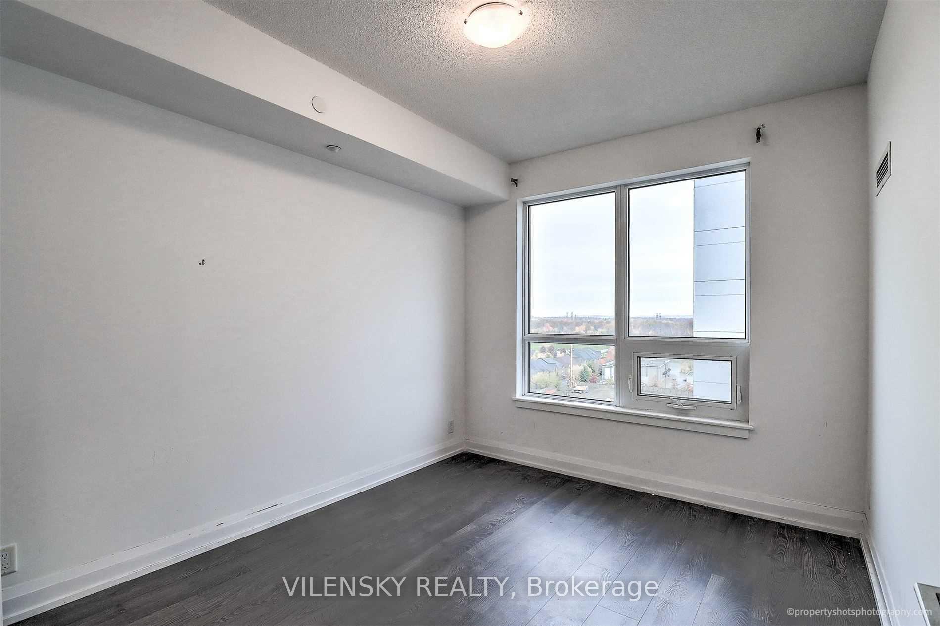Empty room with dark flooring and a large window overlooking rooftops.
