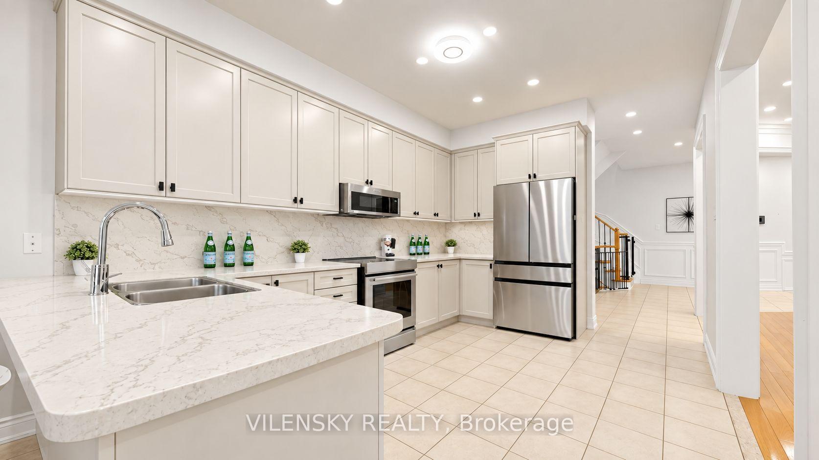 Bright kitchen with white cabinetry, marble-patterned counters, stainless steel appliances, and a large double-sink peninsula.