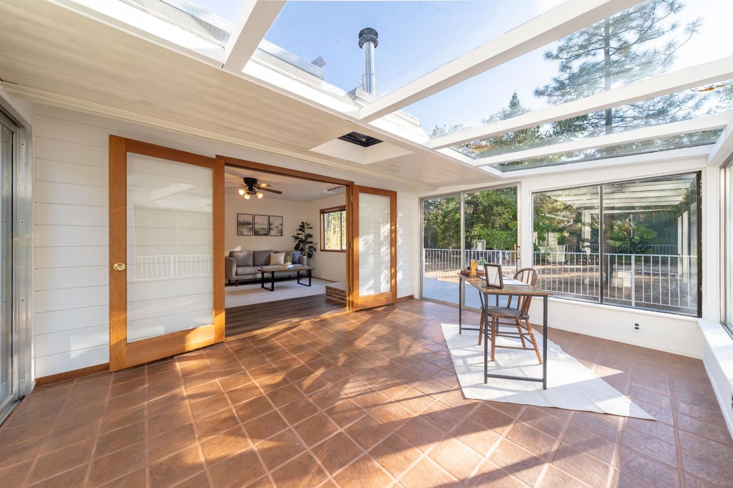 Sunroom with a glass ceiling, tiled floor, and sliding wooden doors opening to a living room.