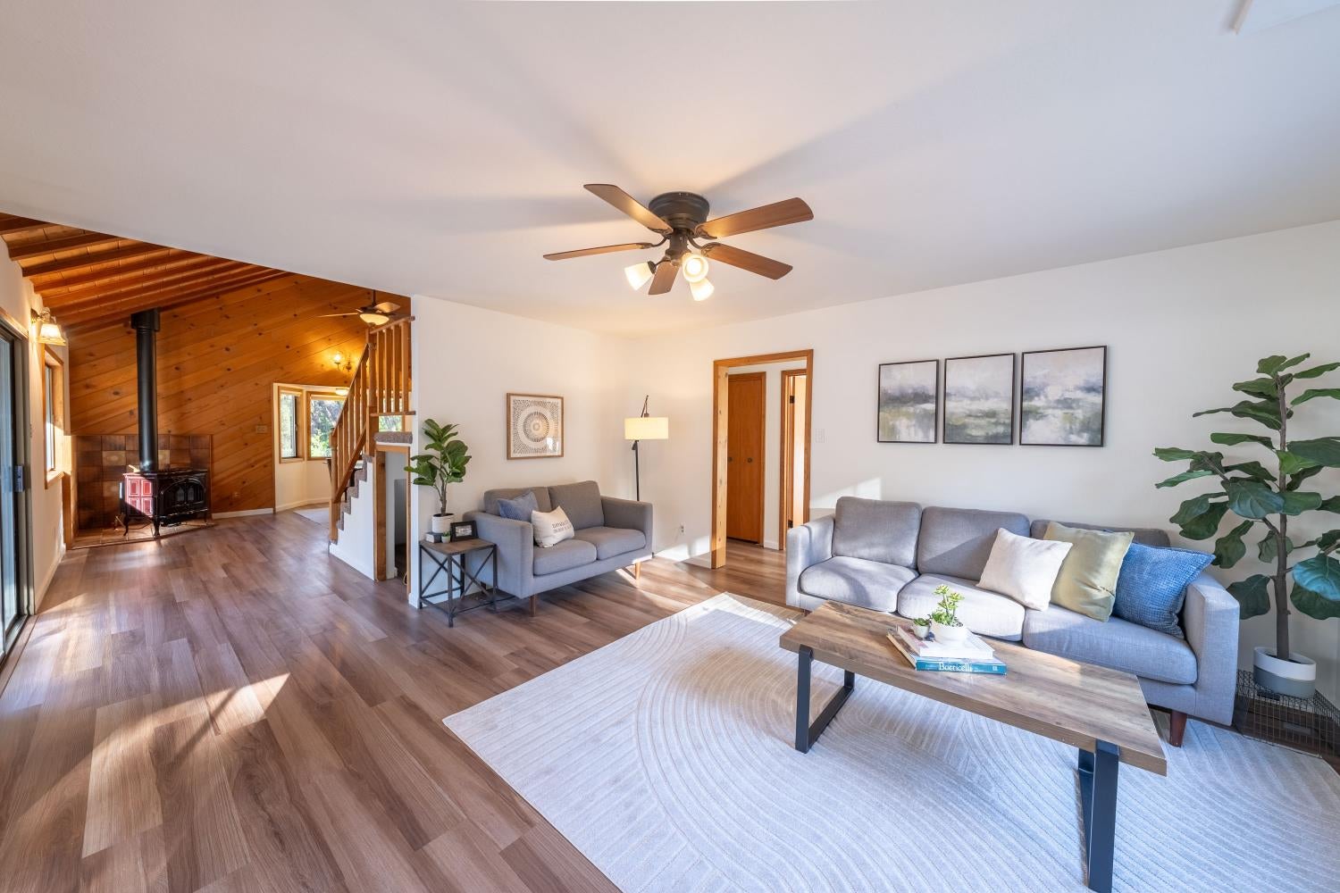Living room with gray sofas and wood flooring, opening to a vaulted wood-paneled area with a stove.