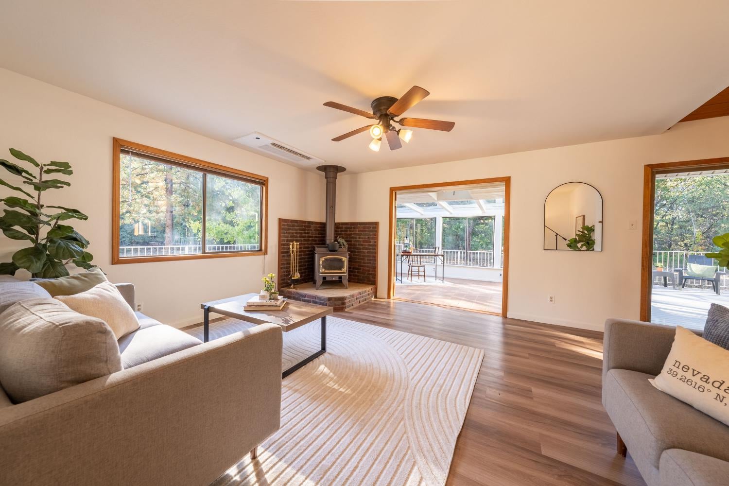 Staged living room with a brick-backed wood stove and open views to a bright porch and wooded deck.