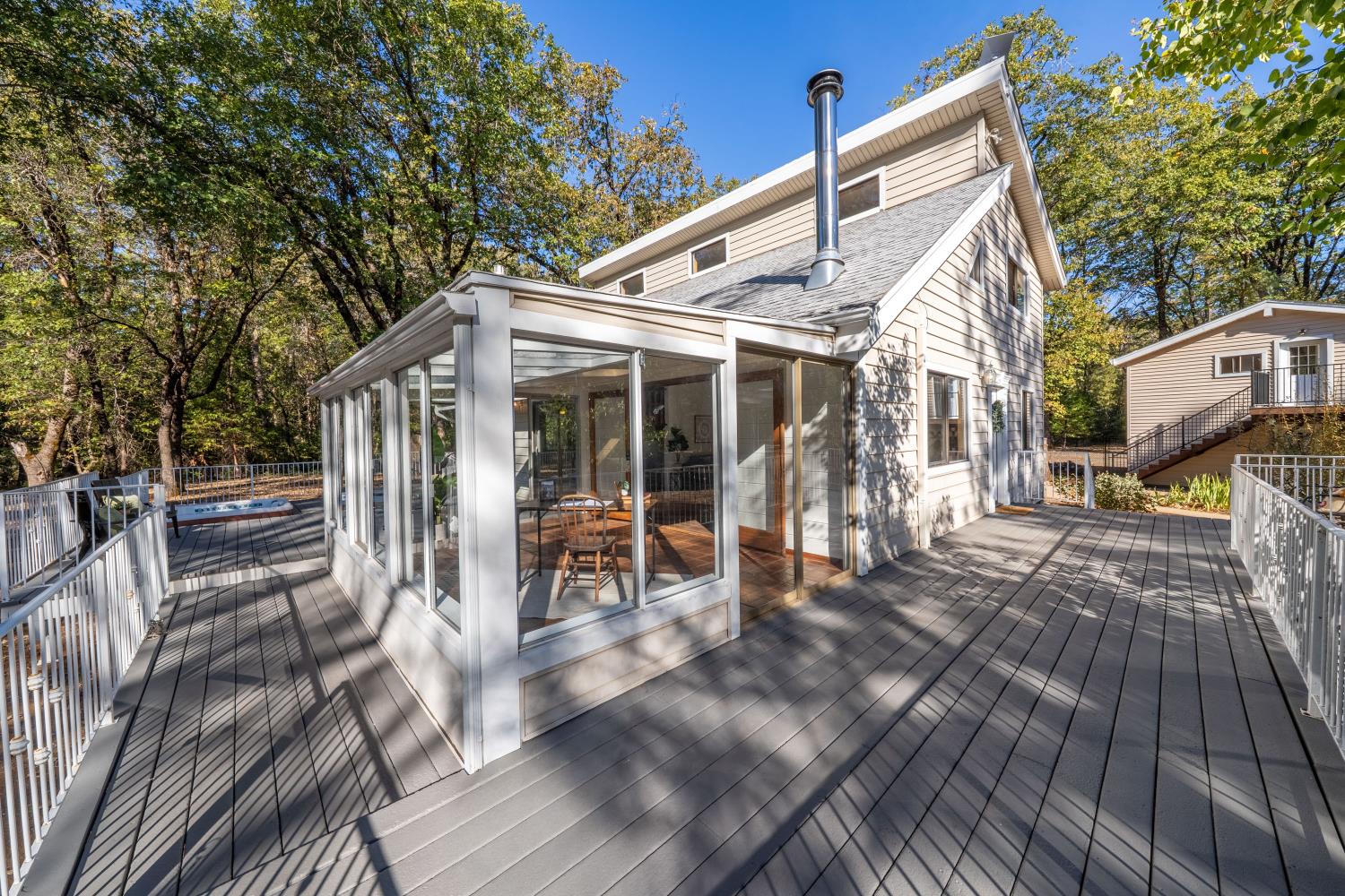 House with a glass-enclosed sunroom and broad deck, surrounded by autumn trees.
