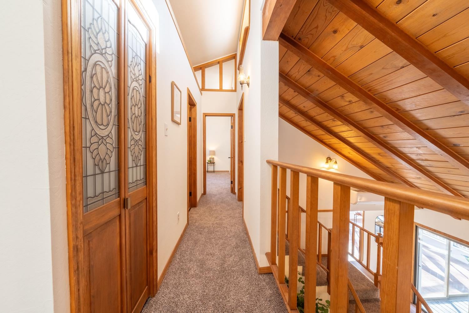 Upstairs hallway with a wood-plank sloped ceiling, patterned glass door, and railing overlooking the lower level.
