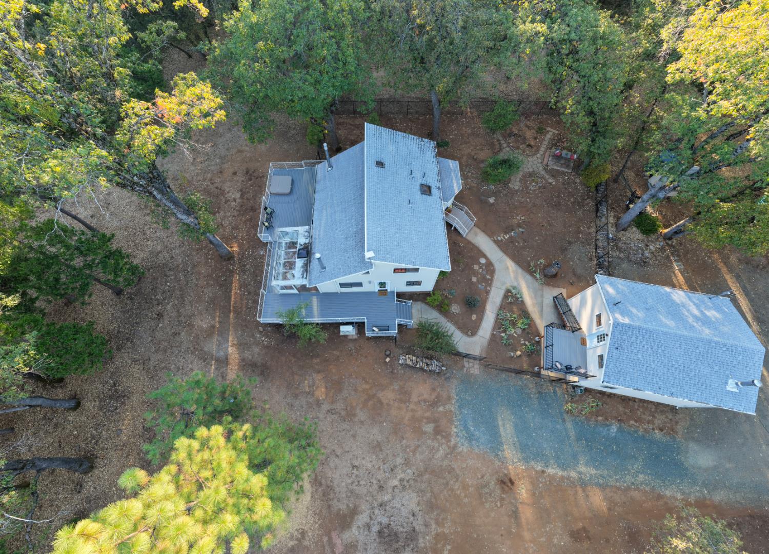 Aerial view of a home among trees, with multiple decks and a curving paved path.