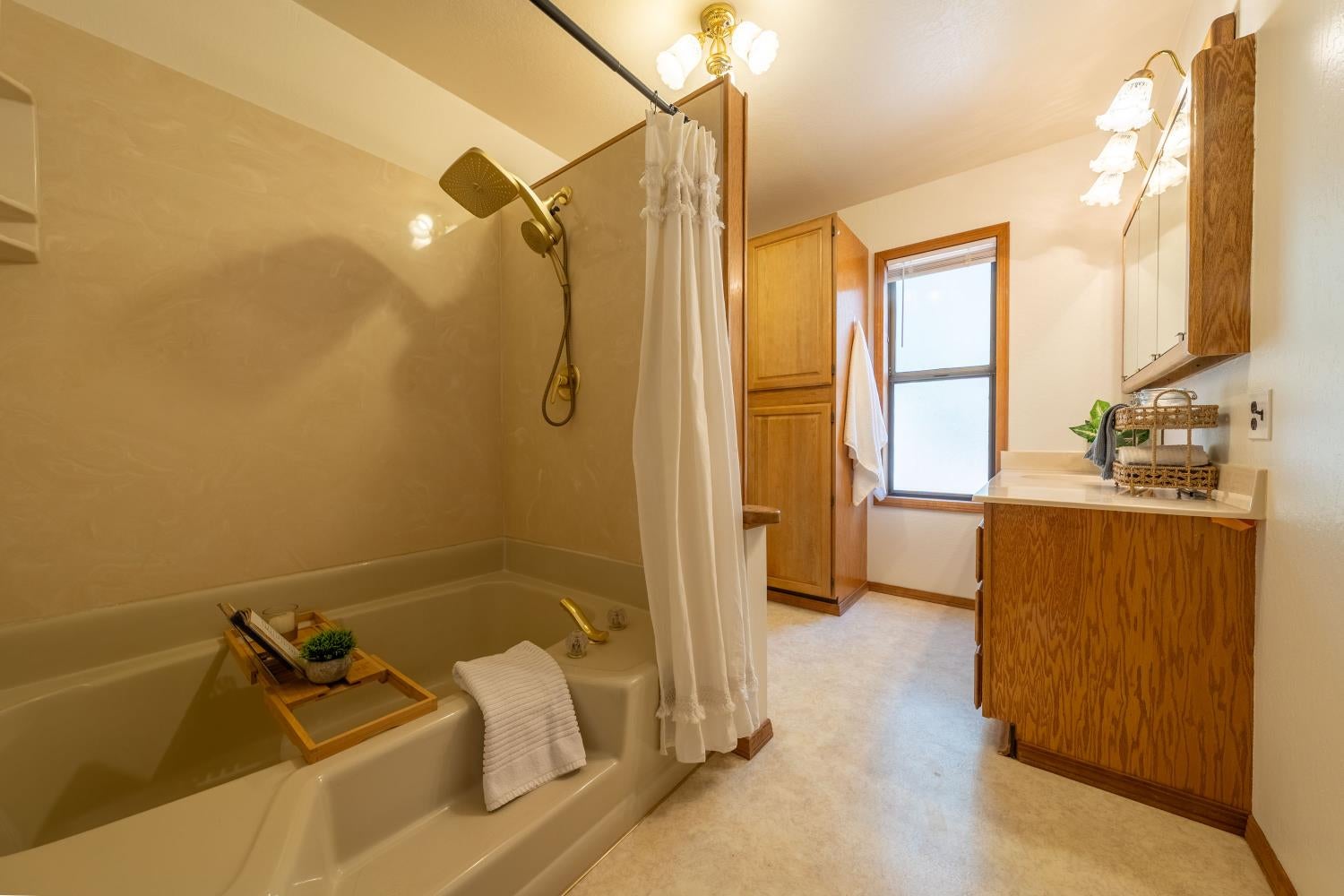 Bathroom with a curtained tub and shower, wood vanity, and window.