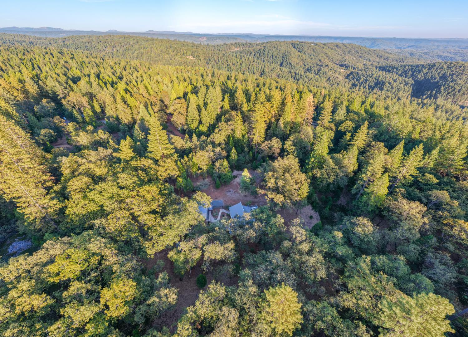Aerial view of a home surrounded by dense forest and distant wooded hills.