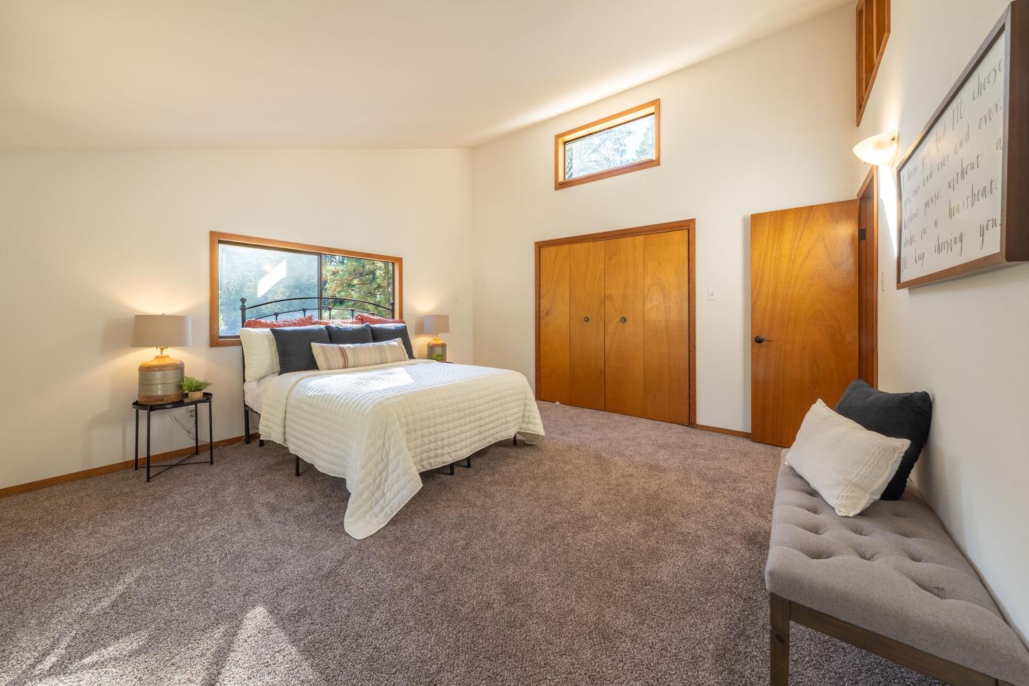 Bedroom with a white quilted bed, warm wood closet doors, and a gray upholstered bench.