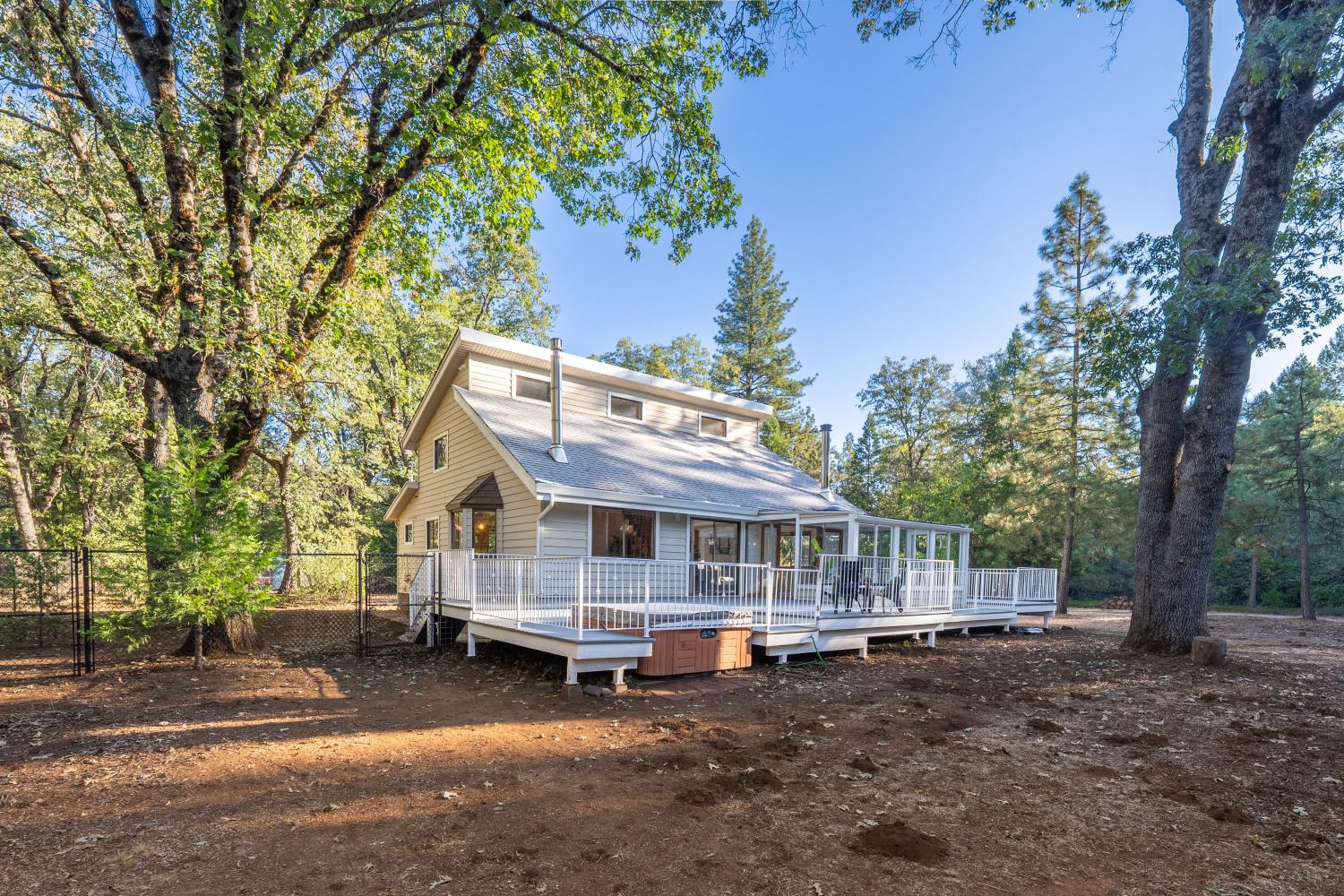 Two-story home with a broad white-railed deck and hot tub beneath mature trees.
