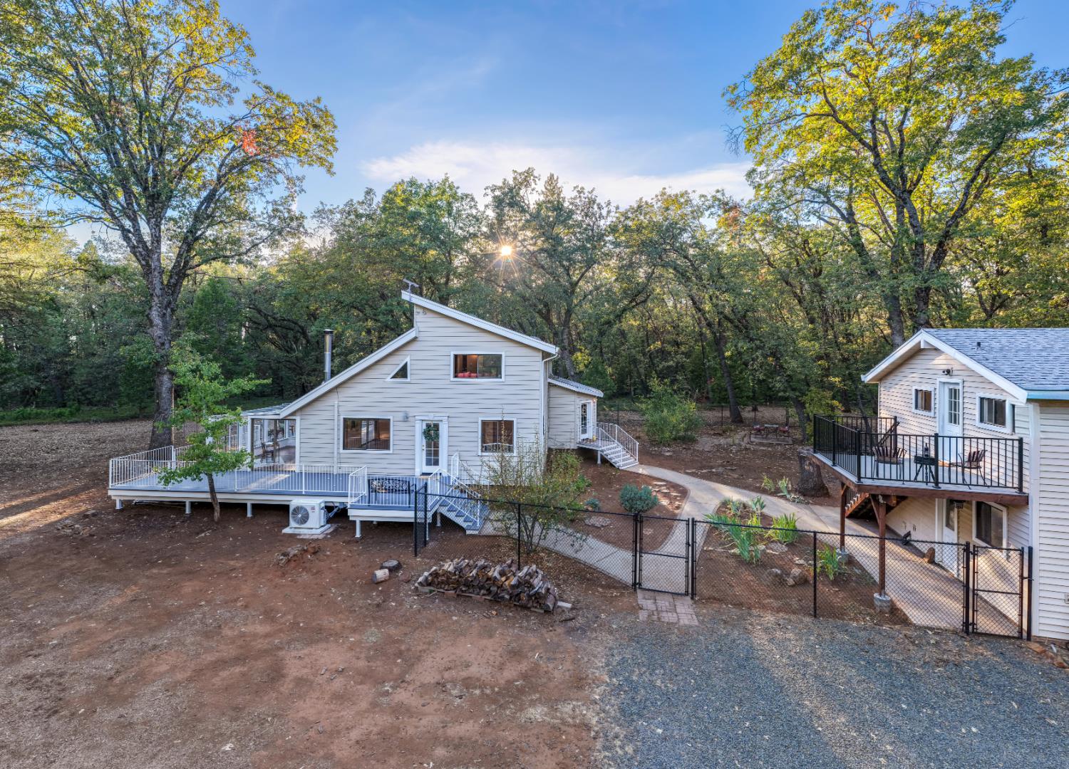 Two light-colored homes with raised decks on a wooded lot.