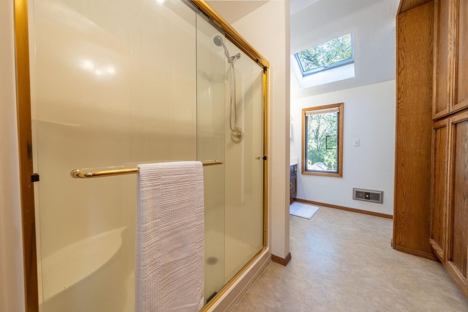 Bathroom with glass-enclosed shower, skylight, and tall wood storage cabinets.