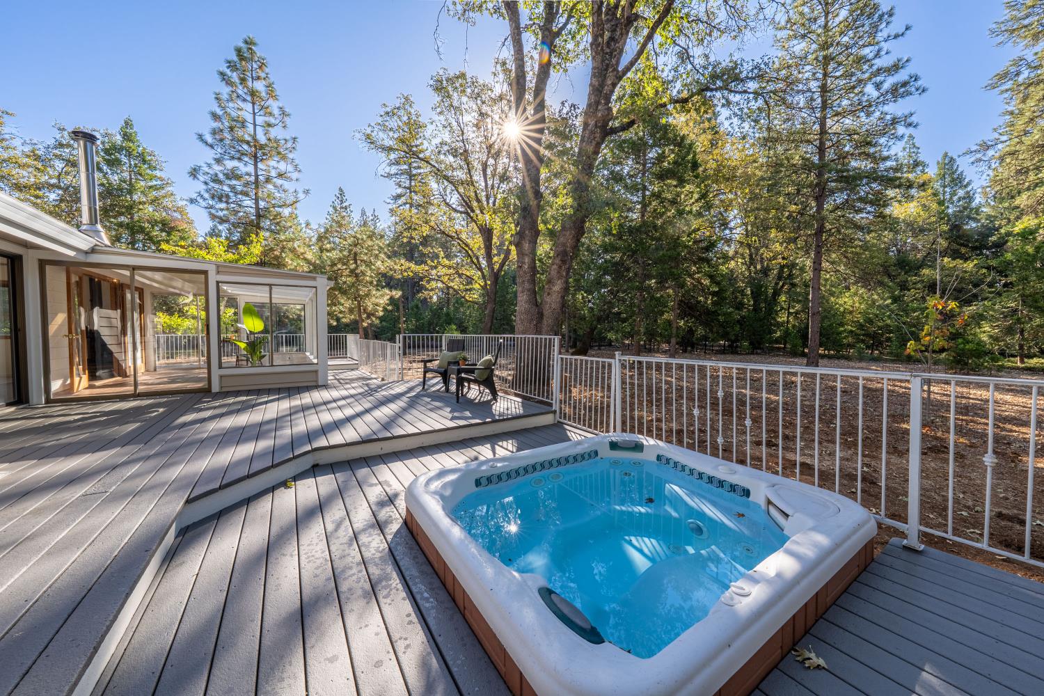 Deck with a built-in hot tub, outdoor seating, and a wooded backdrop.