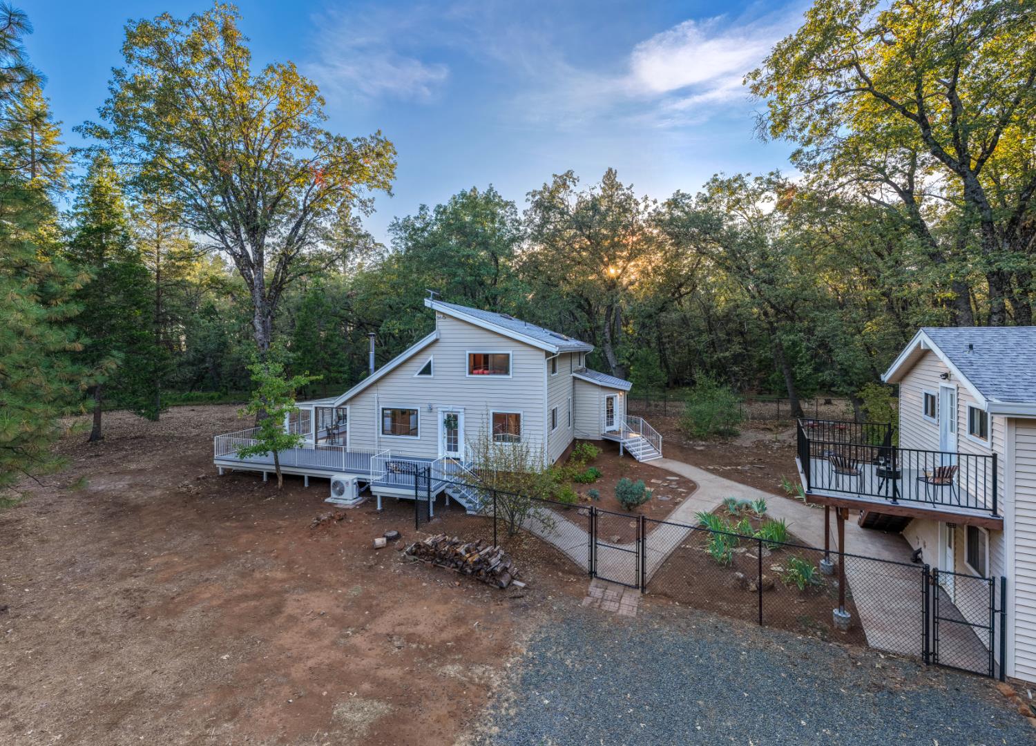 Light-colored home with deck and fenced yard among trees, seen from above.